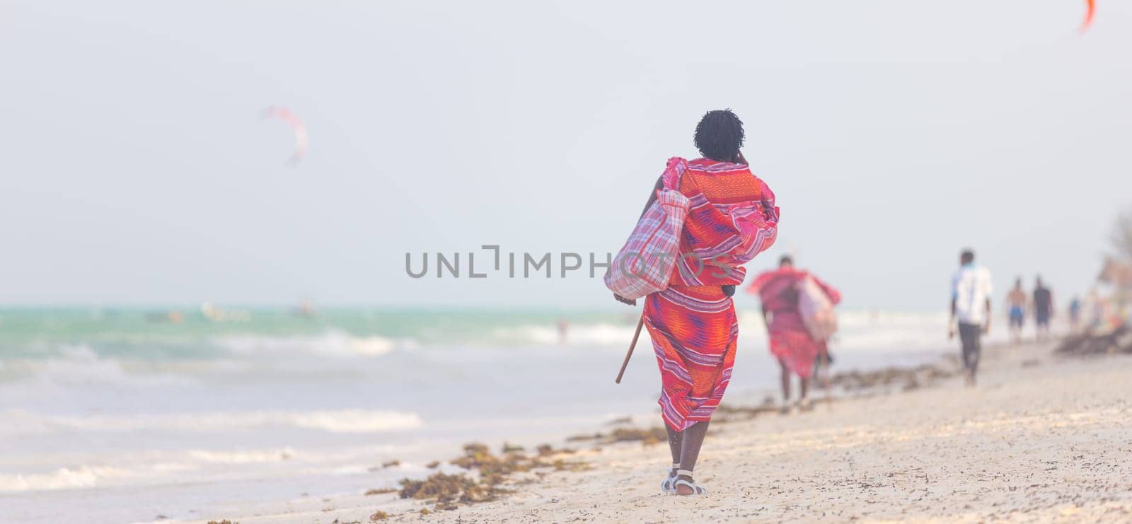 Rear view of traditonaly dressed maasai man walking the sand and selling hand made jewelry on picture perfect tropical Paje beach, Zanzibar, Tanzania, East Africa.