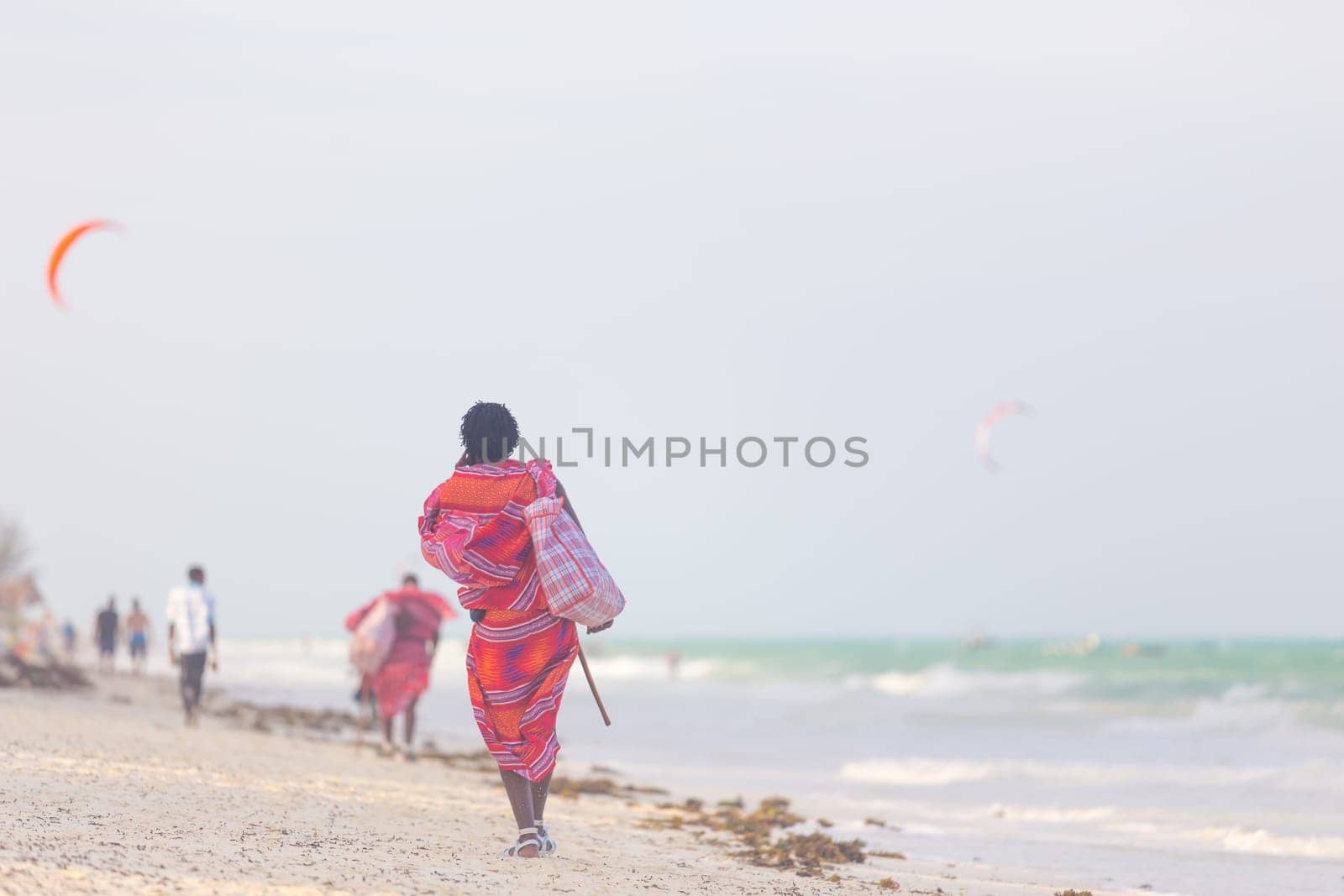 Rear view of traditonaly dressed maasai man walking the sand and selling hand made jewelry on picture perfect tropical Paje beach, Zanzibar, Tanzania, East Africa.