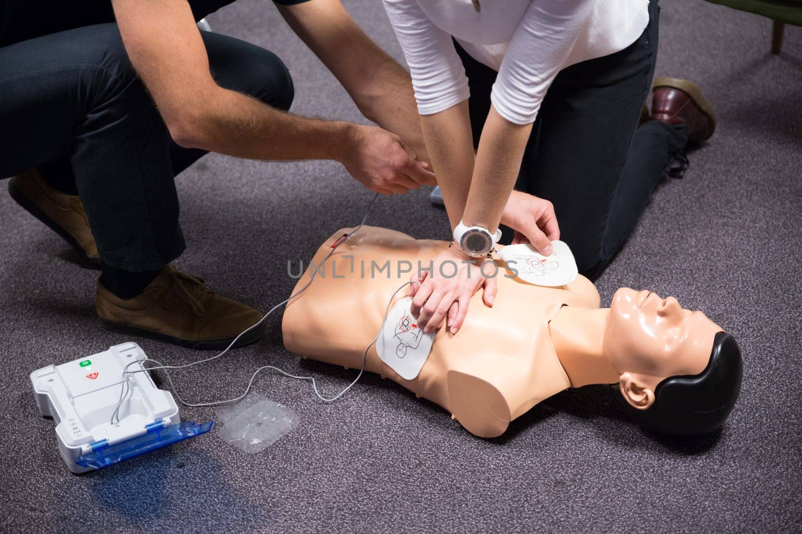 CPR training medical procedure workshop. Demonstrating chest compressions and use of AED automatic defibrillator on CPR doll.