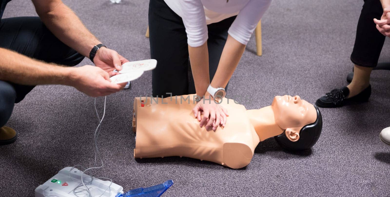CPR training medical procedure workshop. Demonstrating chest compressions and use of AED automatic defibrillator on CPR doll.