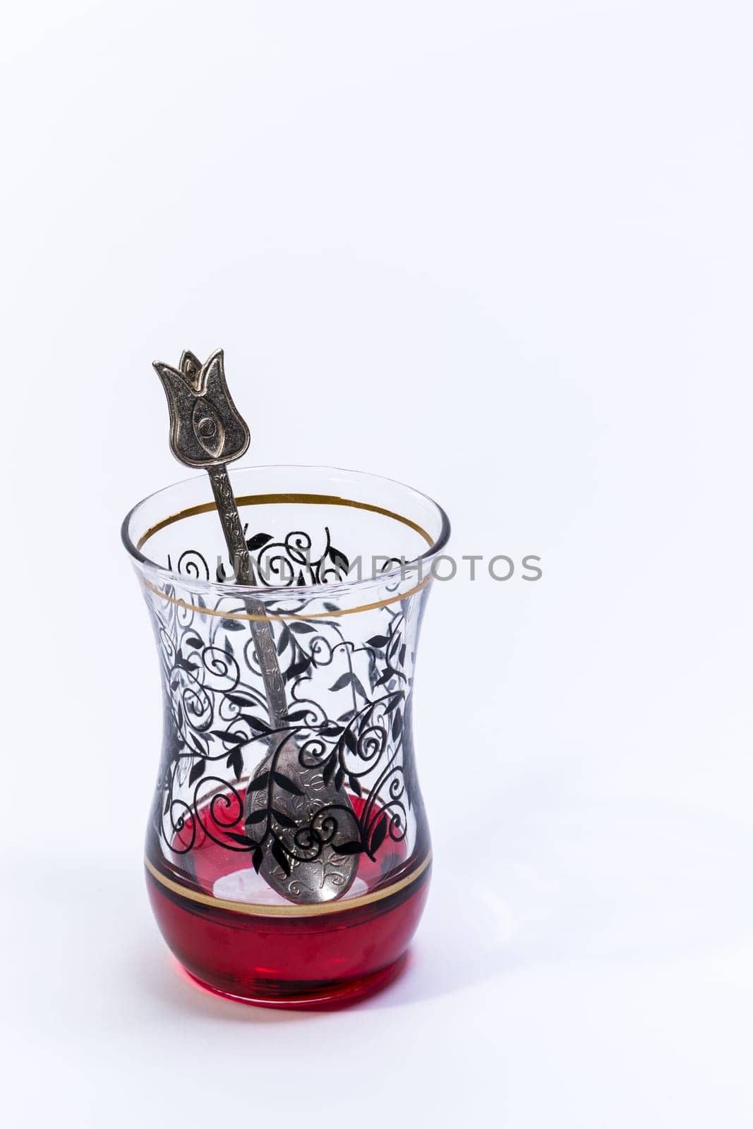 Empty Typical Turkish glass for tea with a teaspoon inside on a white background