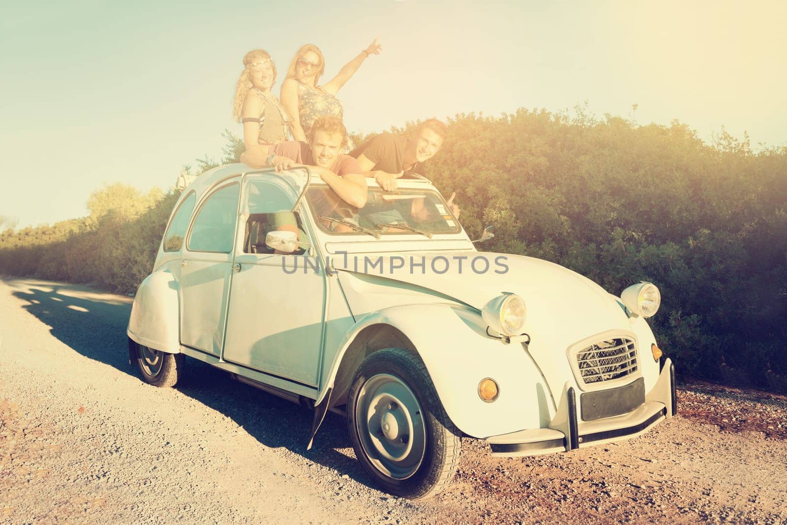 Group of happy friends in a car at sunset in summer.