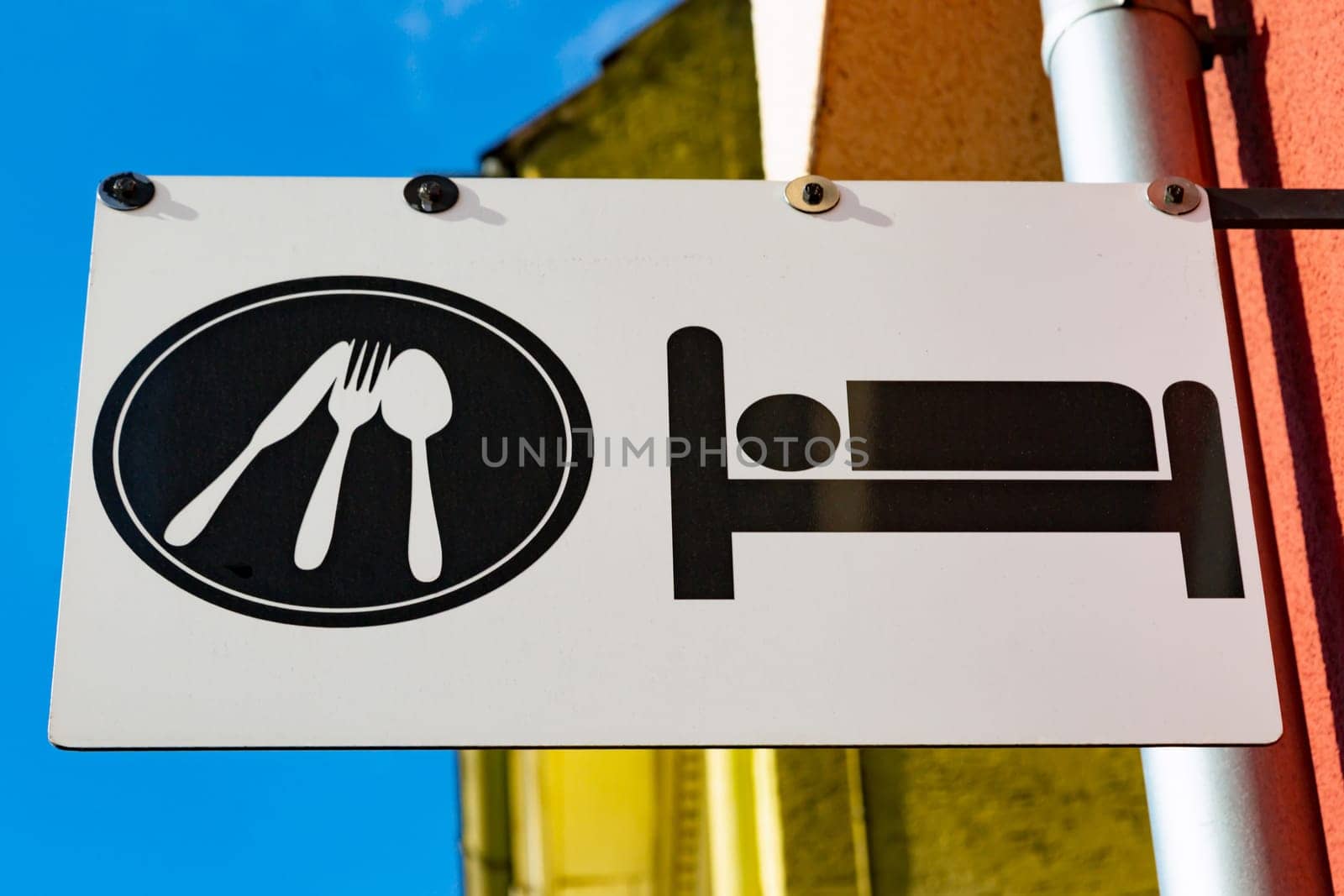 Sign for sleeping accommodation and restaurant on a pole outside a colorful yellow and orange building