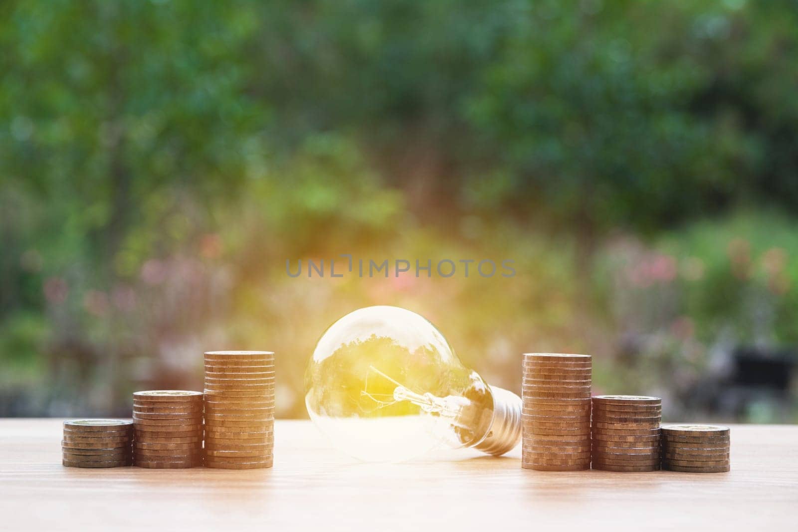 Energy saving light bulb with stacks of coins on nature background.