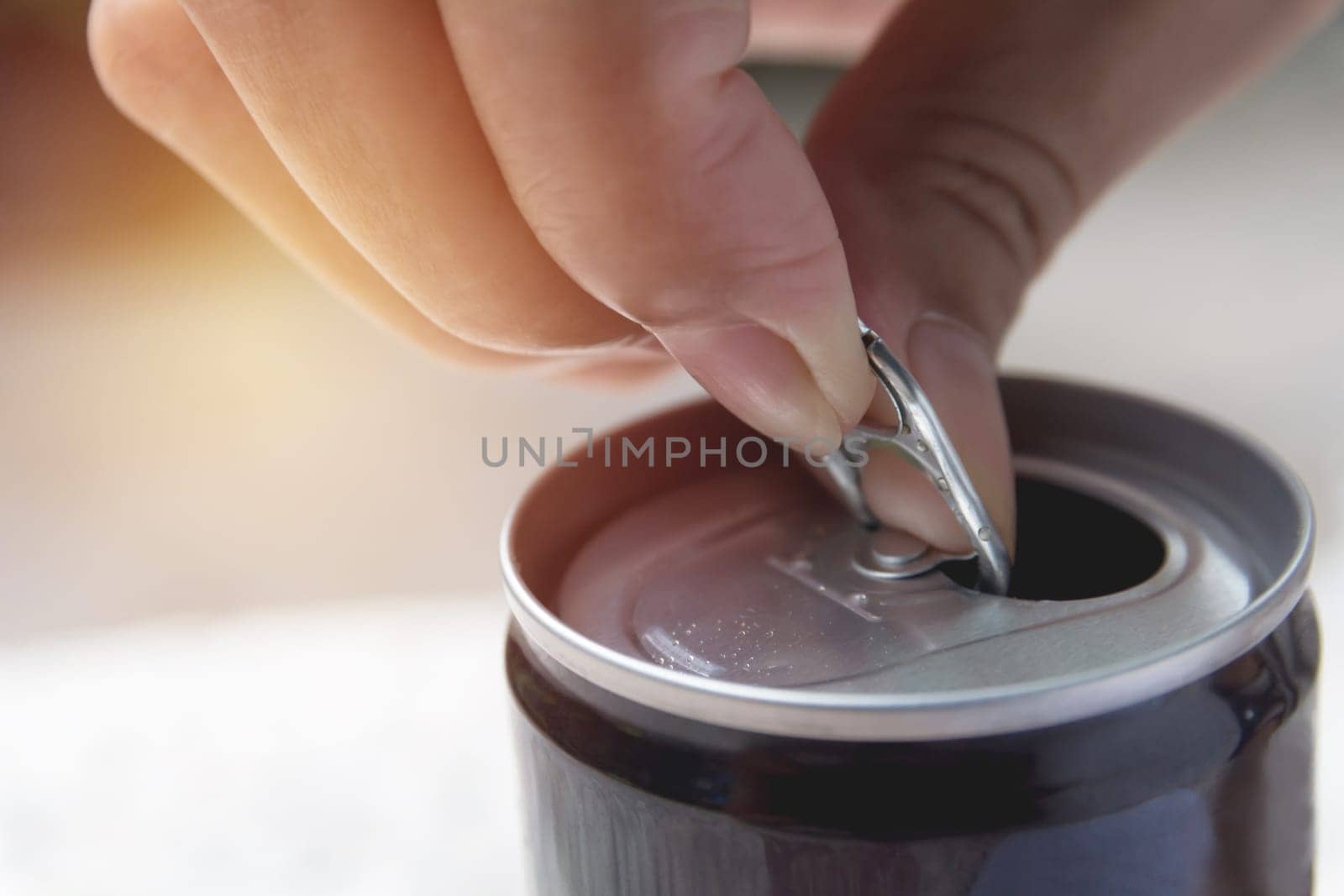 Hand opening an iron can. Can with a drink of cola.