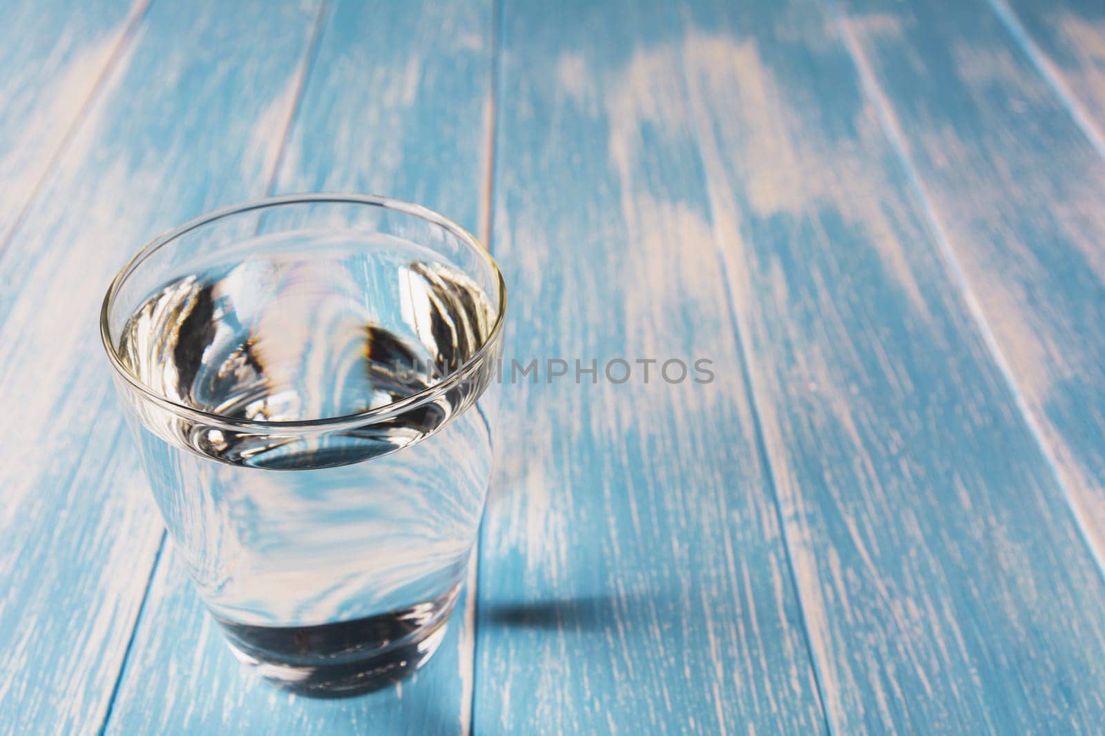 Water in glass on blue and wooden table background.