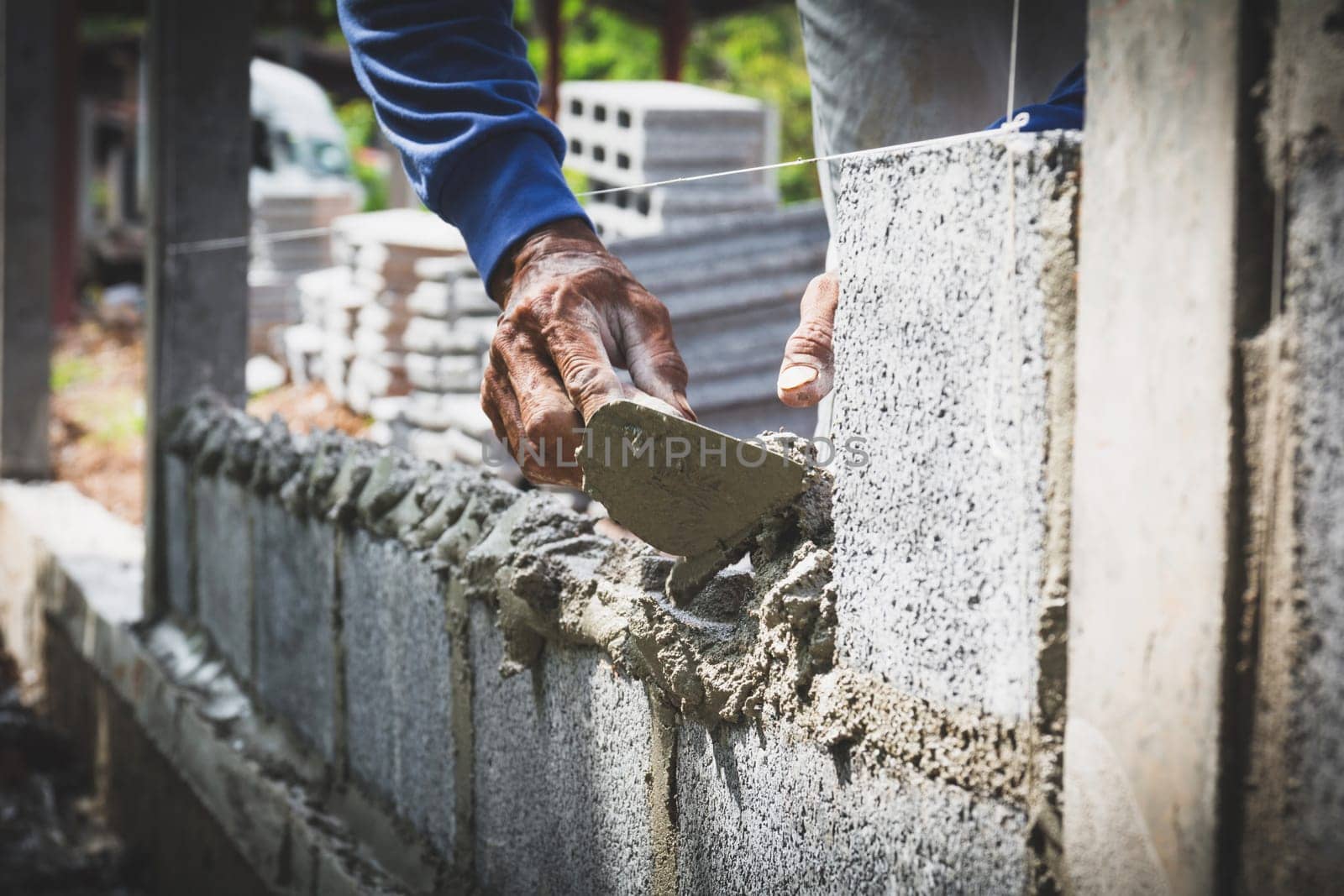 Worker with block concrete cement mortar wall at construction site.