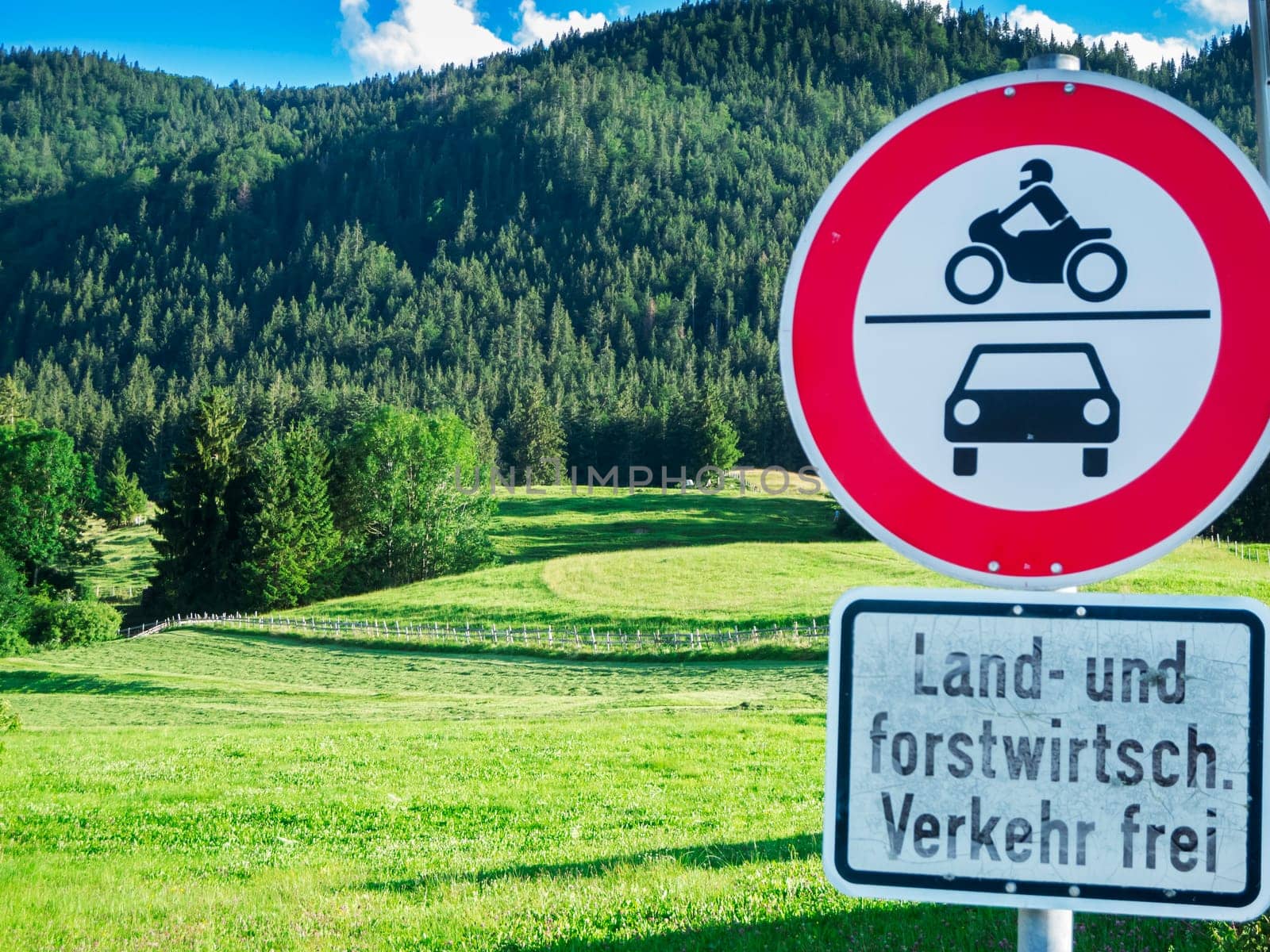 Bavarian mountain landscape with cattle pasture and driving prohibition signs for motor vehicles, except forestry traffic, in the foreground. Focus is on the landscape.