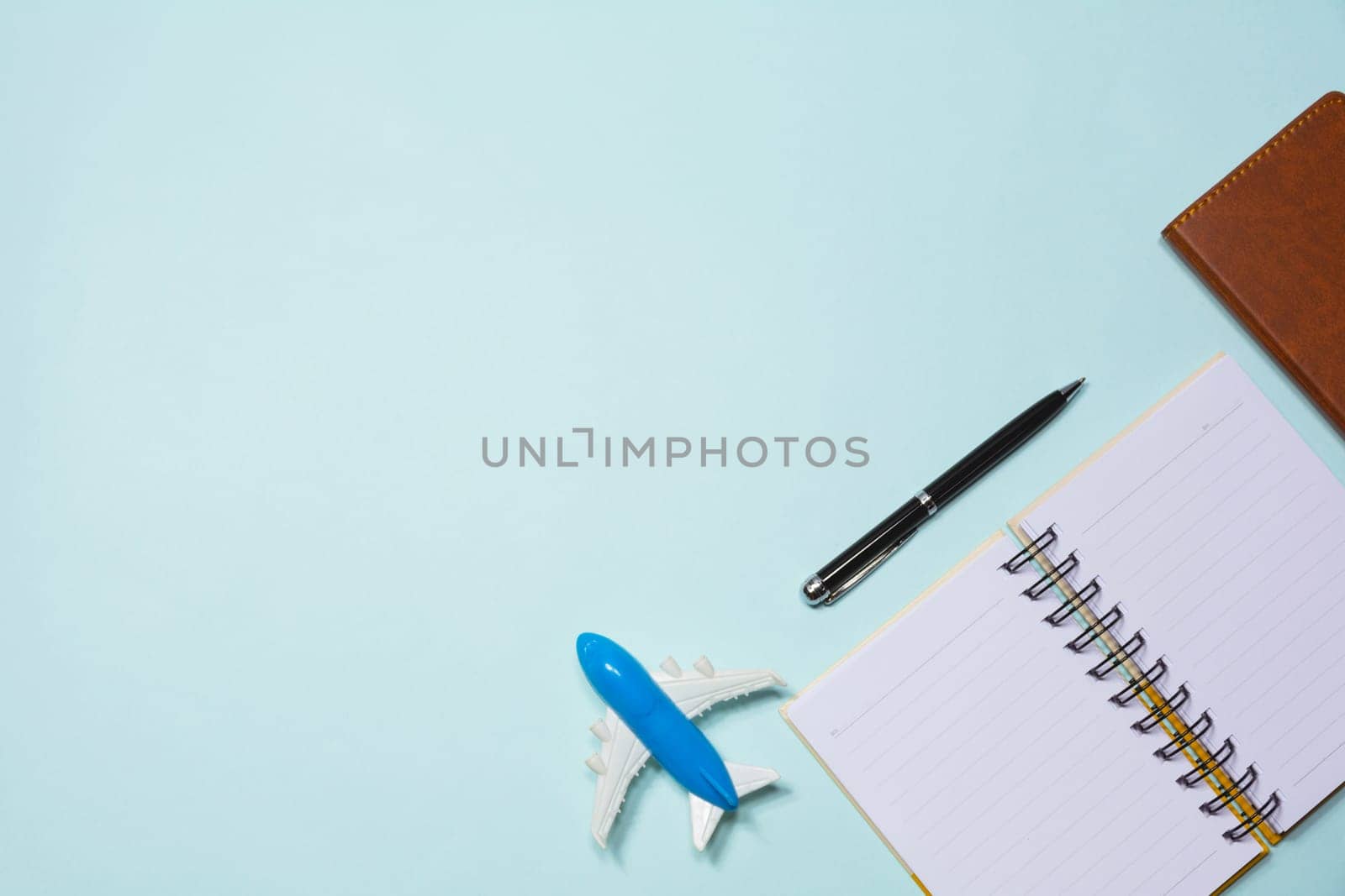 Top view of note book with airplane toy and pen on sky blue background with copy space.