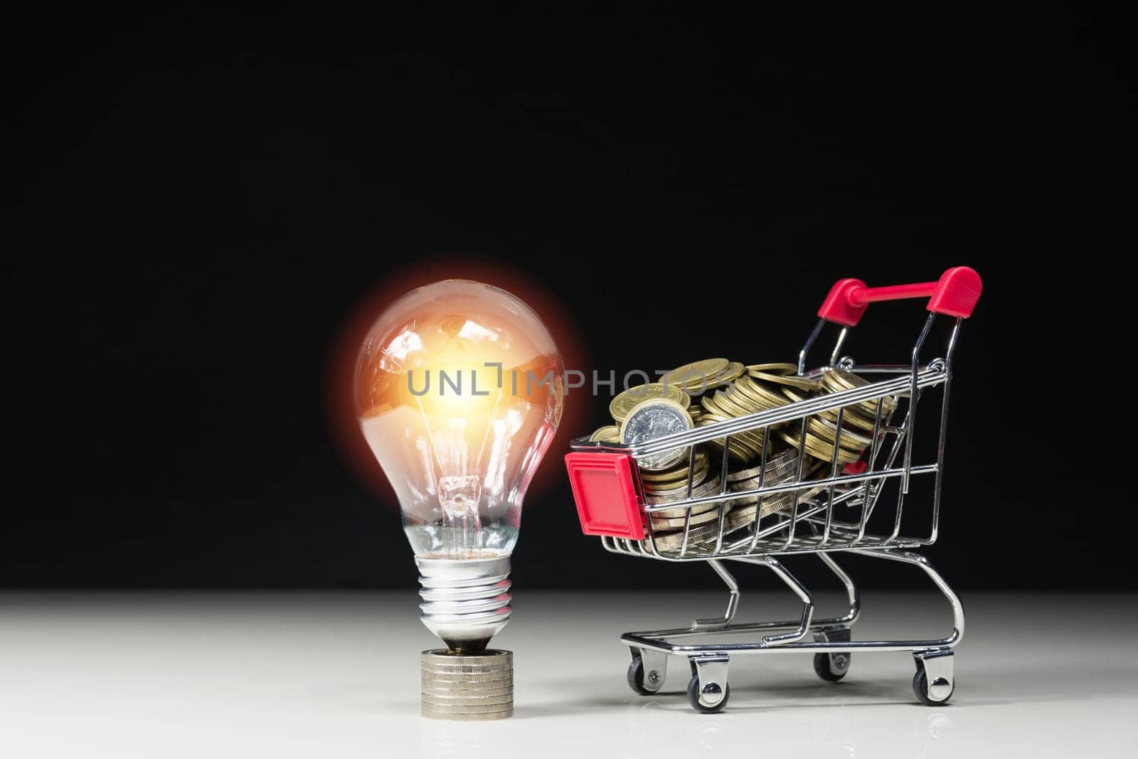 Energy saving light bulb with stacks of coins and shopping cart for saving, financial and shopping concept.