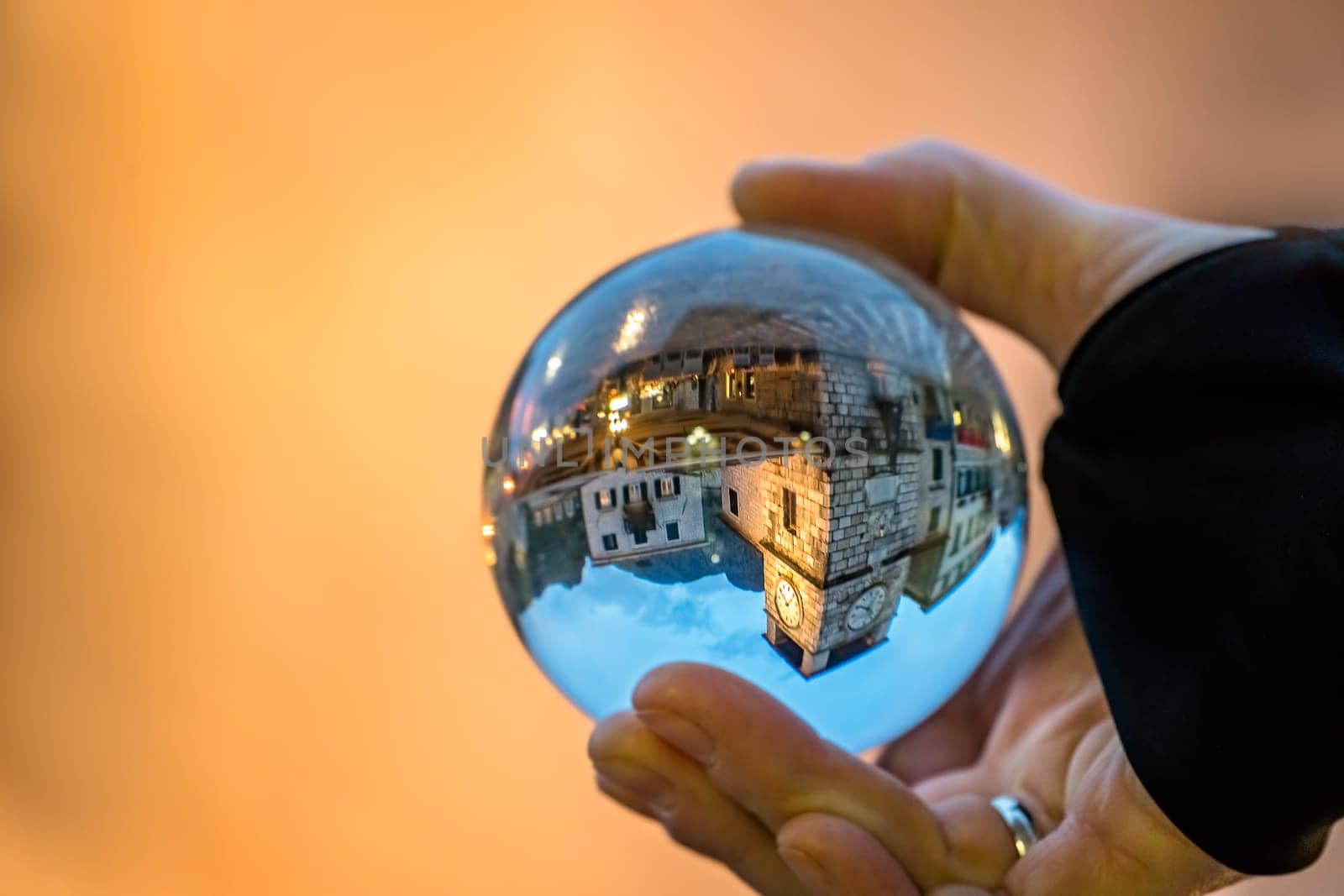 Man holding transparent glass ball reflecting the old Clock tower and square in Kotor Old Town, Montenegro