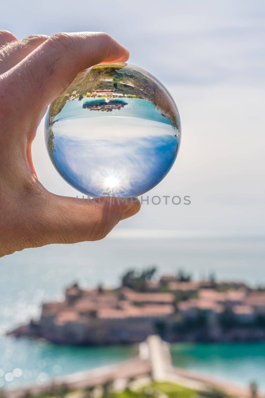 Historical Sveti Stefan old town reflected in large transparent glass ball, coast of Montenegro