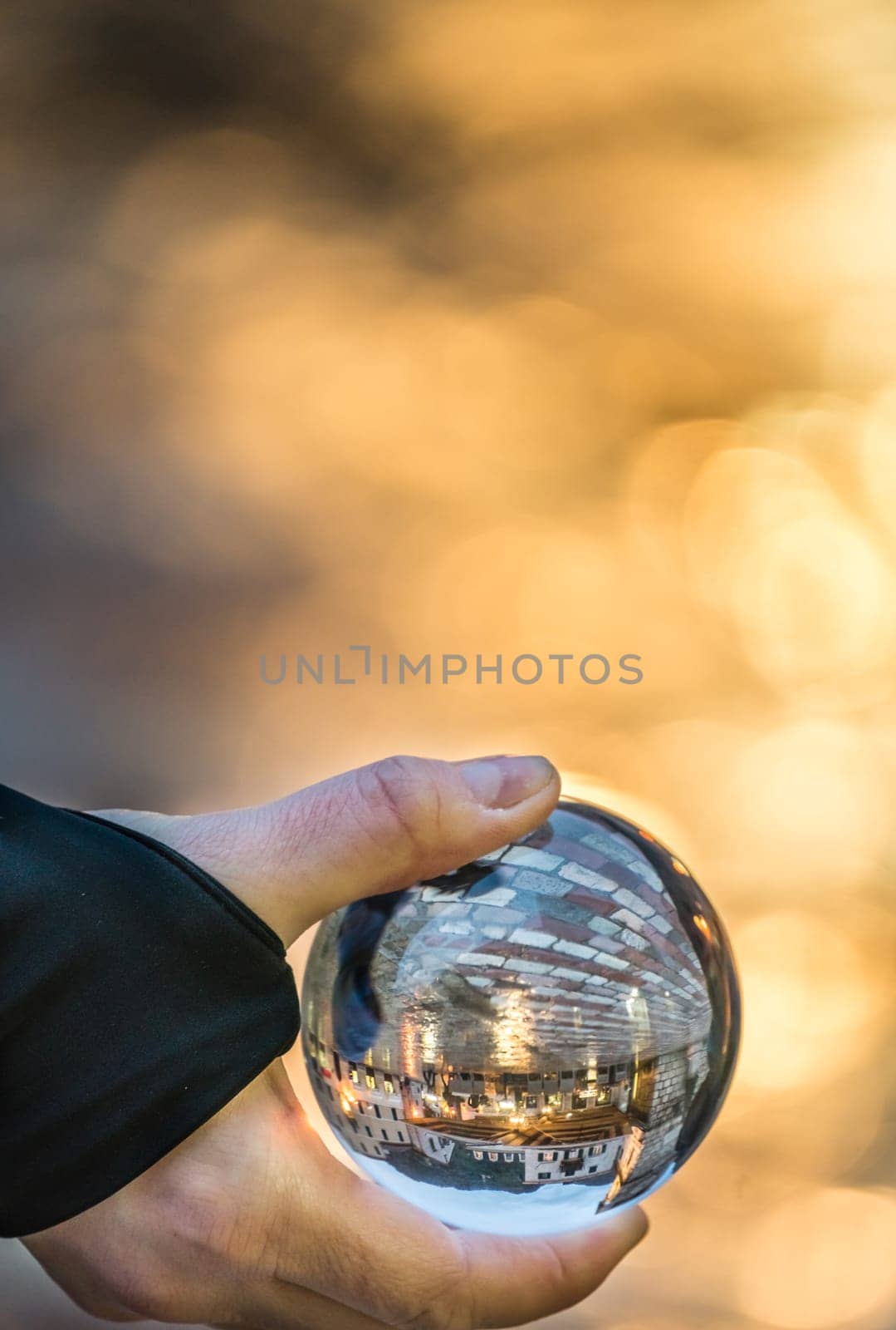 Man holding transparent glass ball reflecting the old Clock tower and square in Kotor Old Town, Montenegro