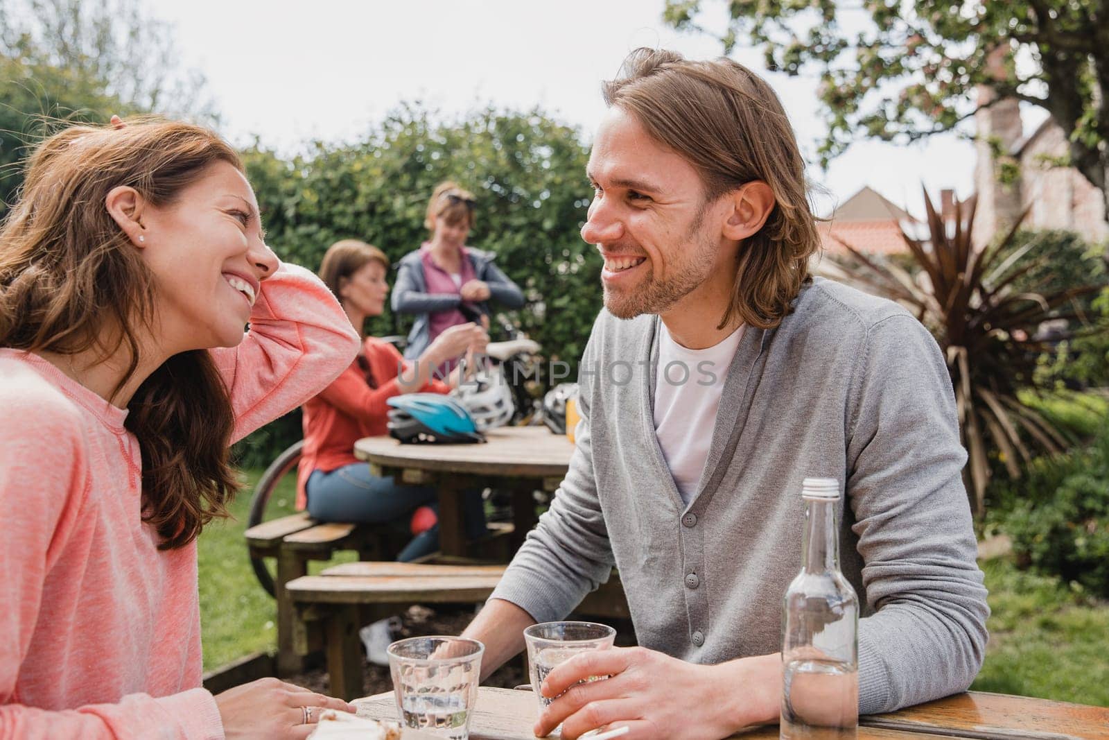 Mid-adult couple sitting at a bench outdoors in a public park. They are looking at each other, smiling, laughing and talking.