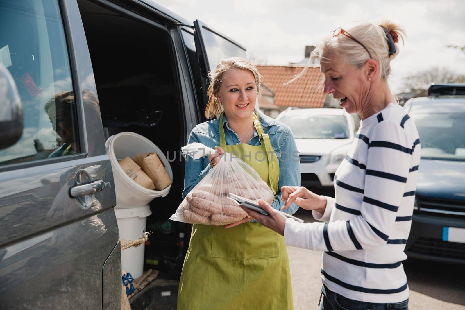 Mature female adult collecting a delivery off a young female adult outside from a delivery van.