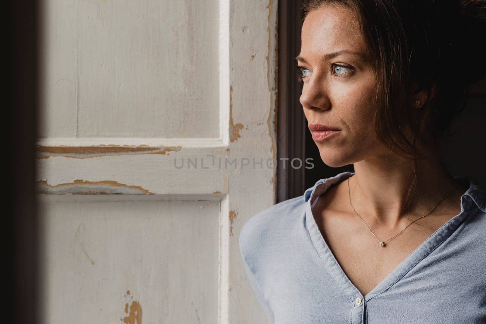 Mid adult woman standning at a wooden framed window looking out.