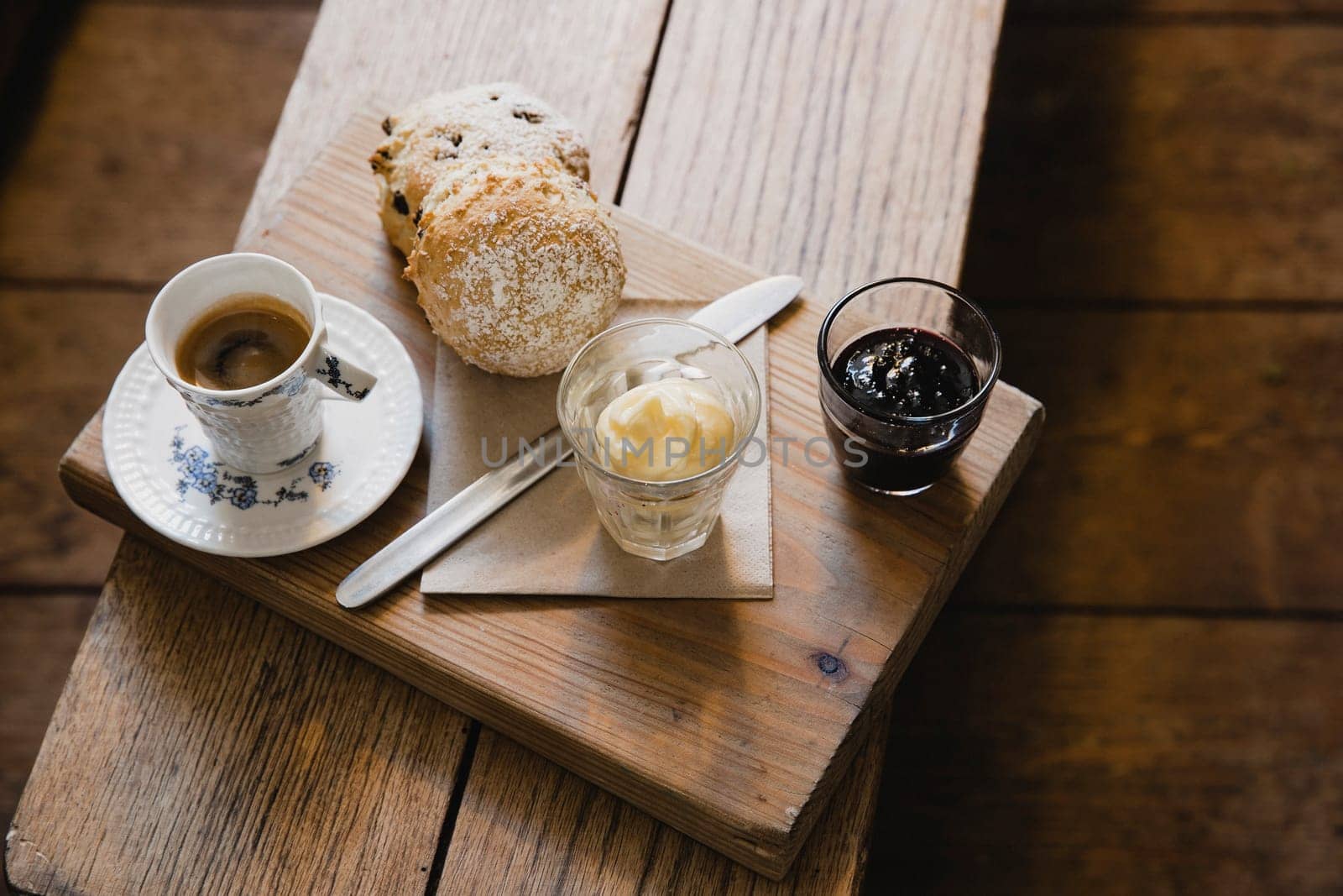 High angle view of a espresso coffee and scone on a wooden seat. There is some clotted cream and strawberry jam for the scone.