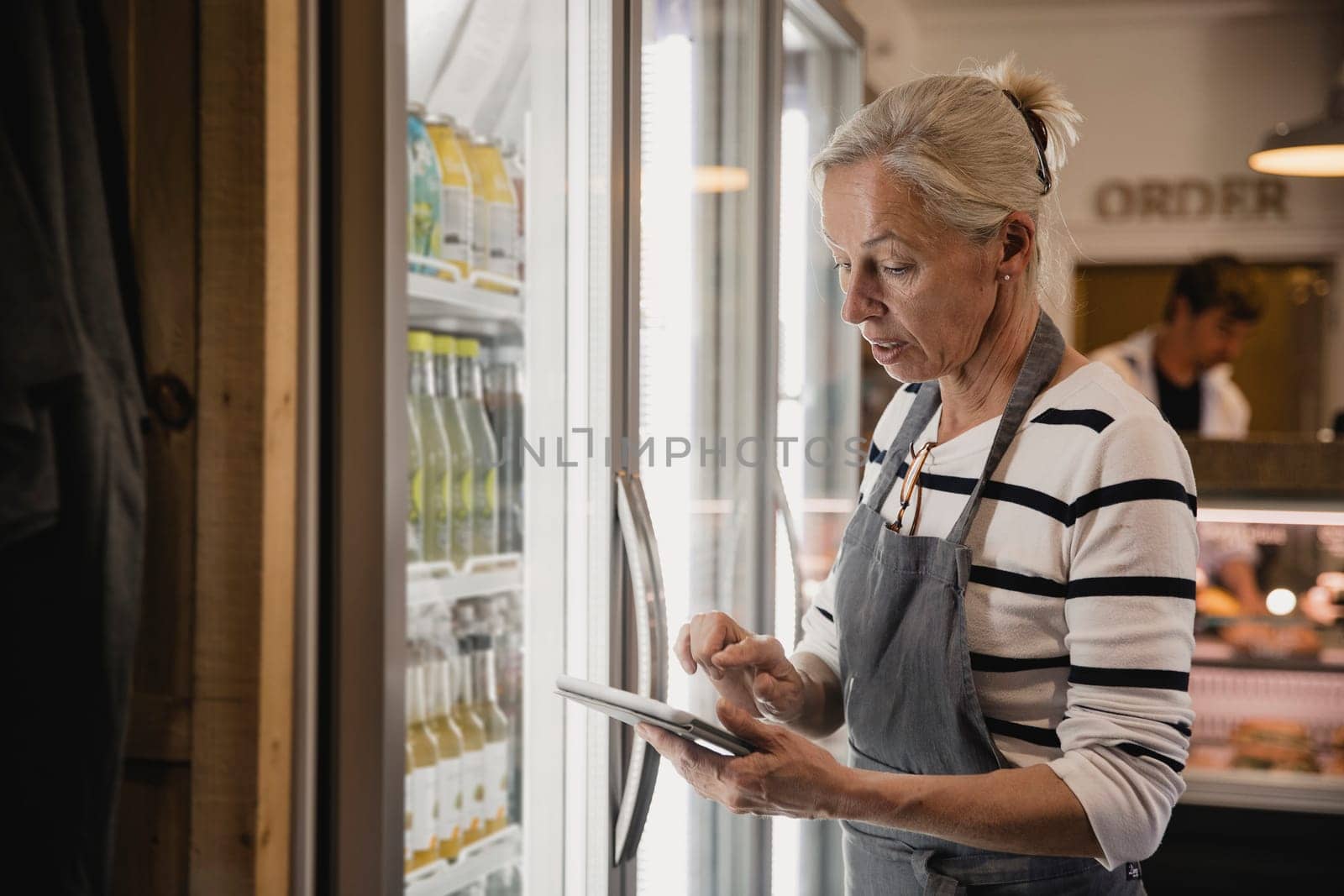 Mature coffee shop employee standing next to the fridges in the coffee shop performing a stock take.