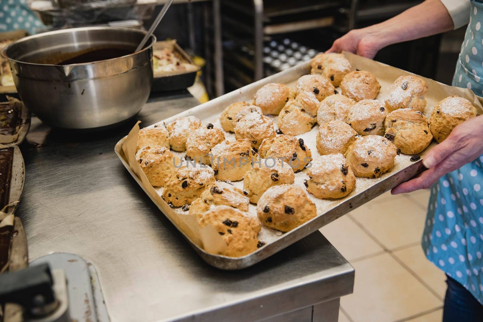 Unrecognisable person placing a tray of fruit scones on the worktop in the kitchen.