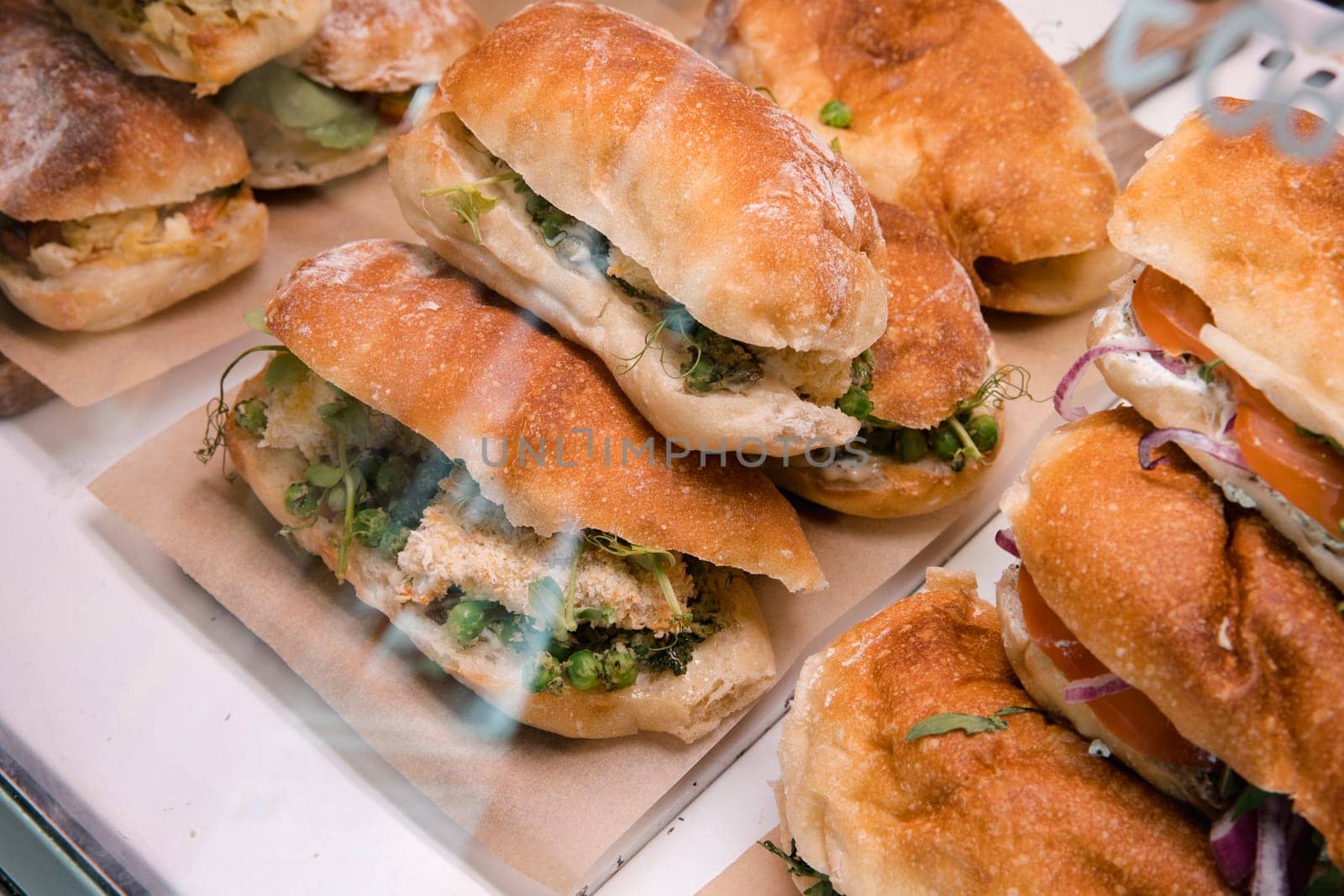 Stack of sandwiches in a coffee shop display cabinet. There is a variety to choose from.