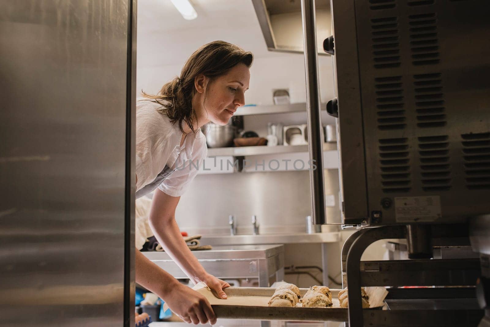 Mid adult female baker placing a tray of uncooked scones into the oven.