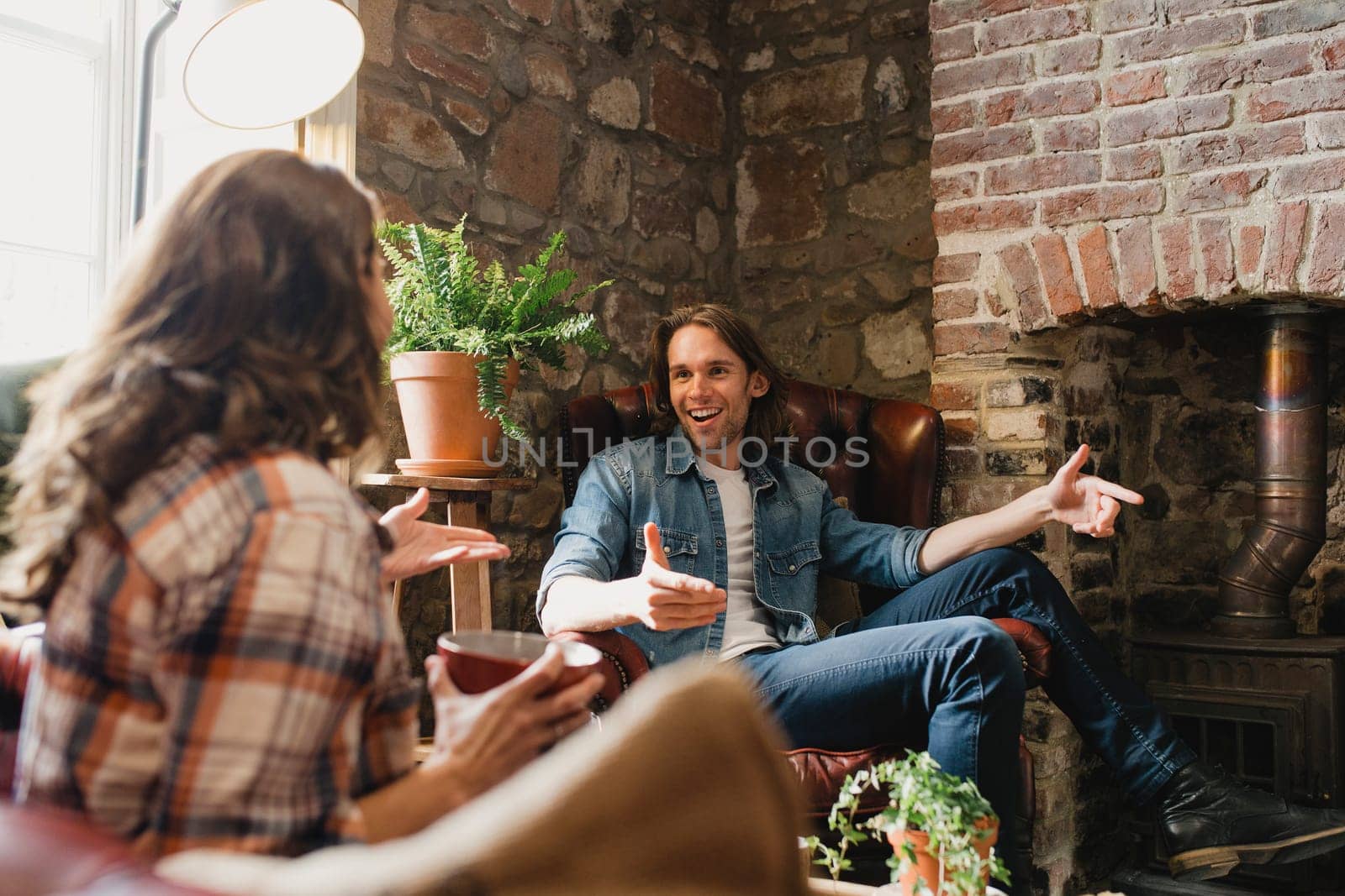Mid-adult couple sitting in a small coffee shop relaxing. They are sitting on leather sofas and enjoying a coffee while talking.