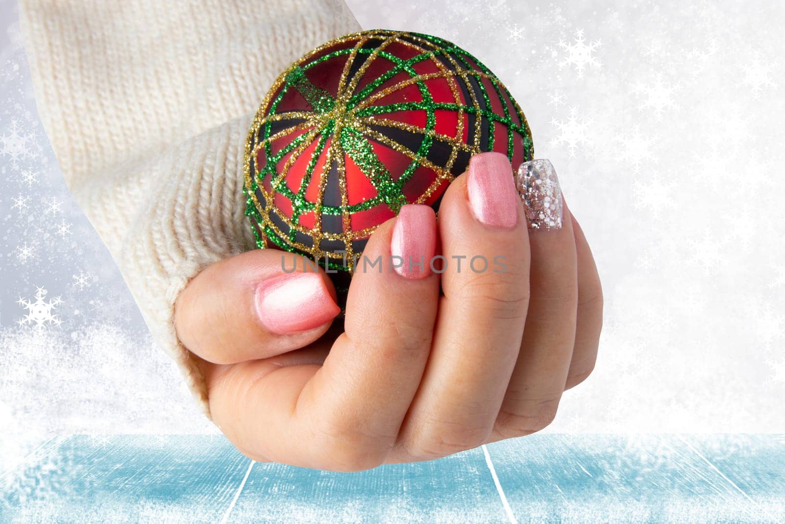 Beautiful female hand with christmas nail design. Hand with elegant pink nail manicure holding a red christmas decoration ball. Space for advertising.