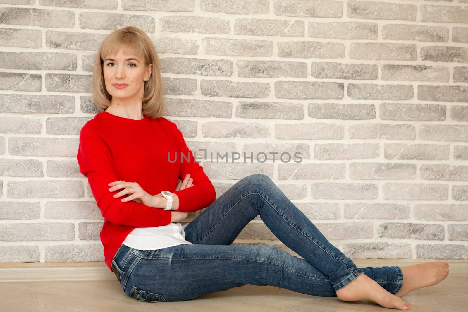 Happy girl smiling. Young happy positive woman in shirt sitting on floor in room on wall background. European woman. Positive human emotions facial expression body language