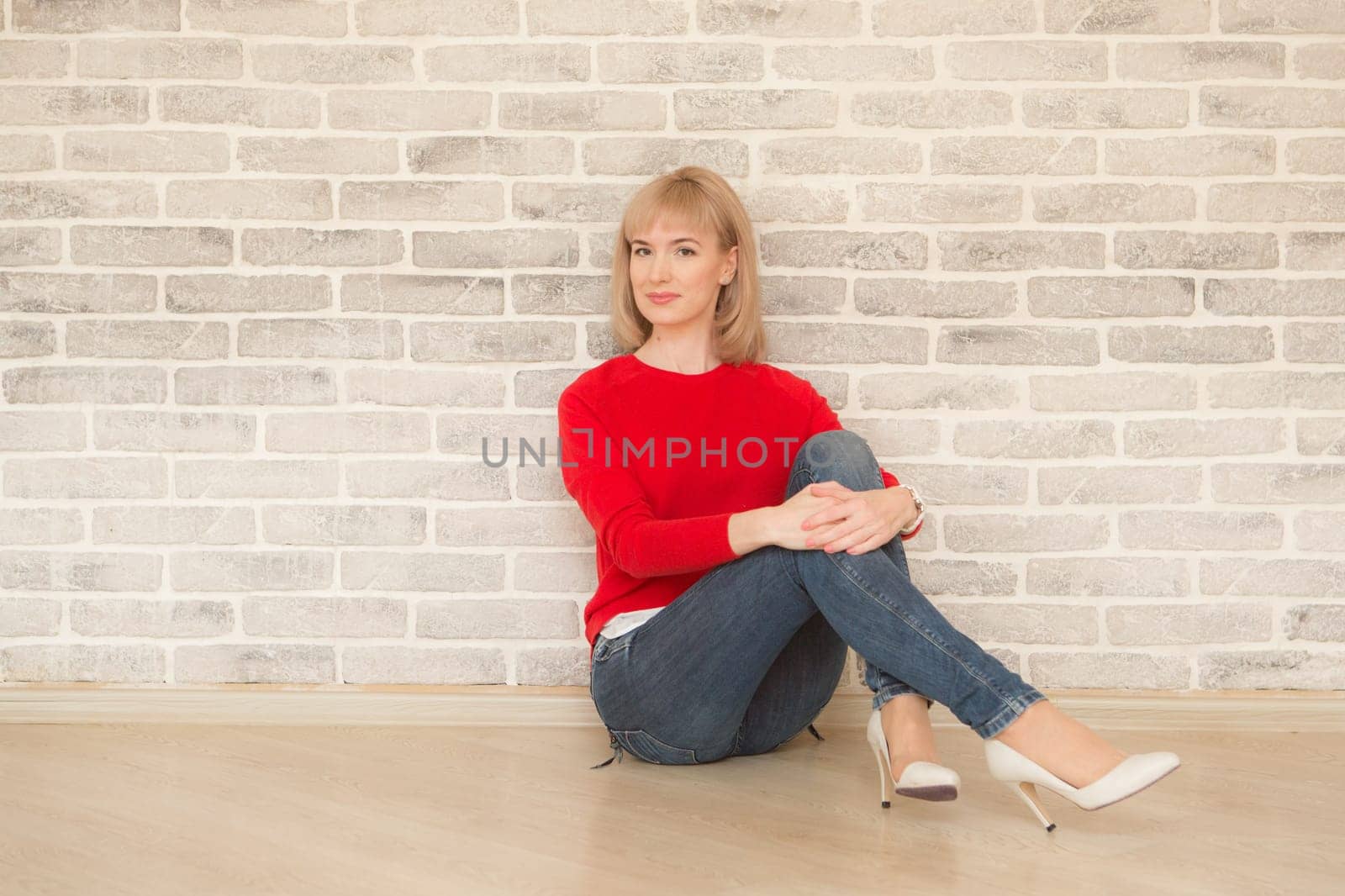 Happy girl smiling. Young happy positive woman in shirt sitting on floor in room on wall background. European woman. Positive human emotions facial expression body language