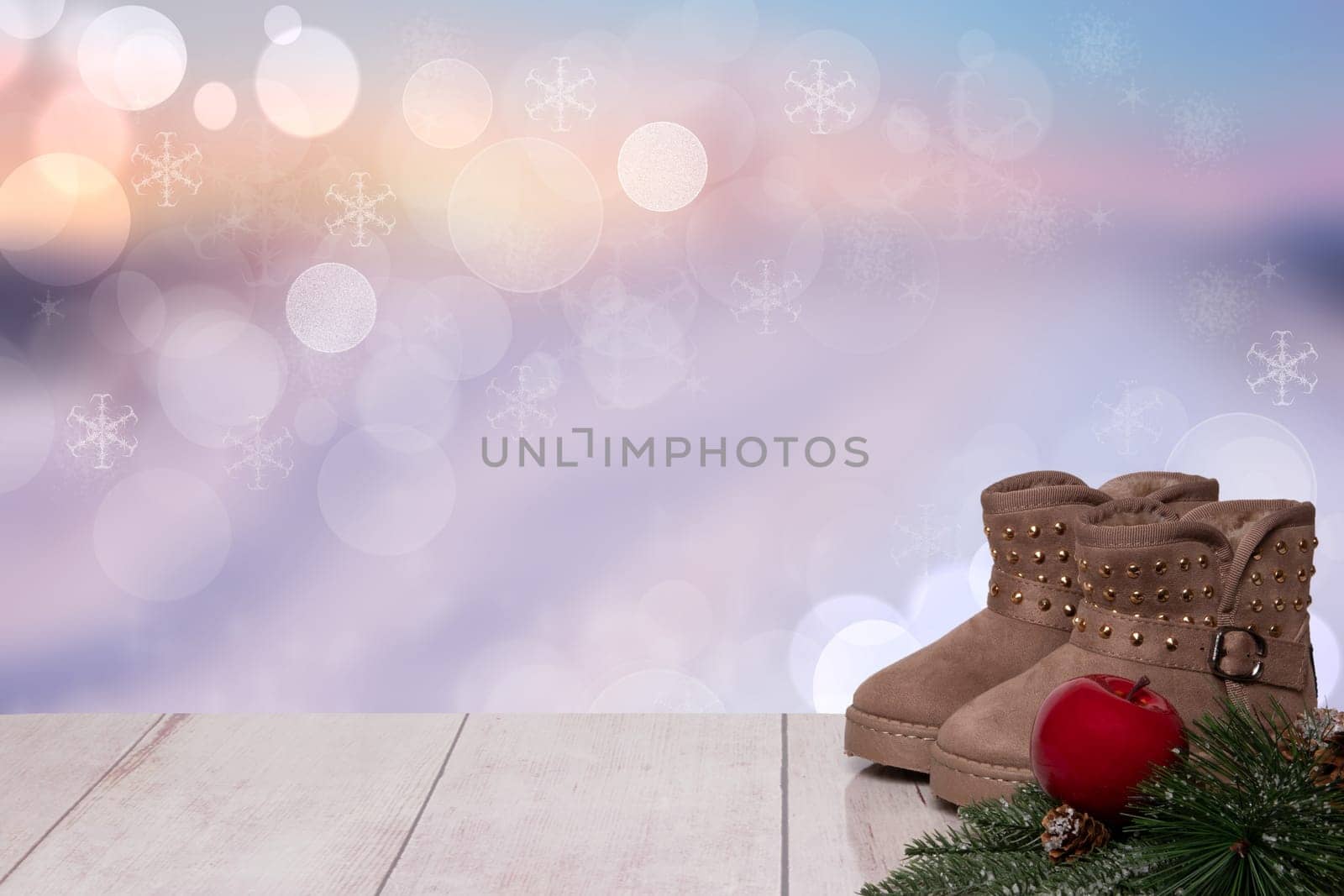Christmas background. Table top christmas winter decoration background with an pair of winter boots and xmas tree fir branches and an red apple over beautiful abstract purple christmas background. Space for design. Card concept.