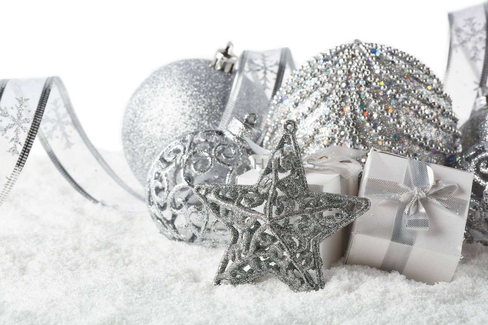 Christmas still life with silver balls, star and gift boxes lying on winter snow on a white background. Horizontal view. New Year and Christmas.