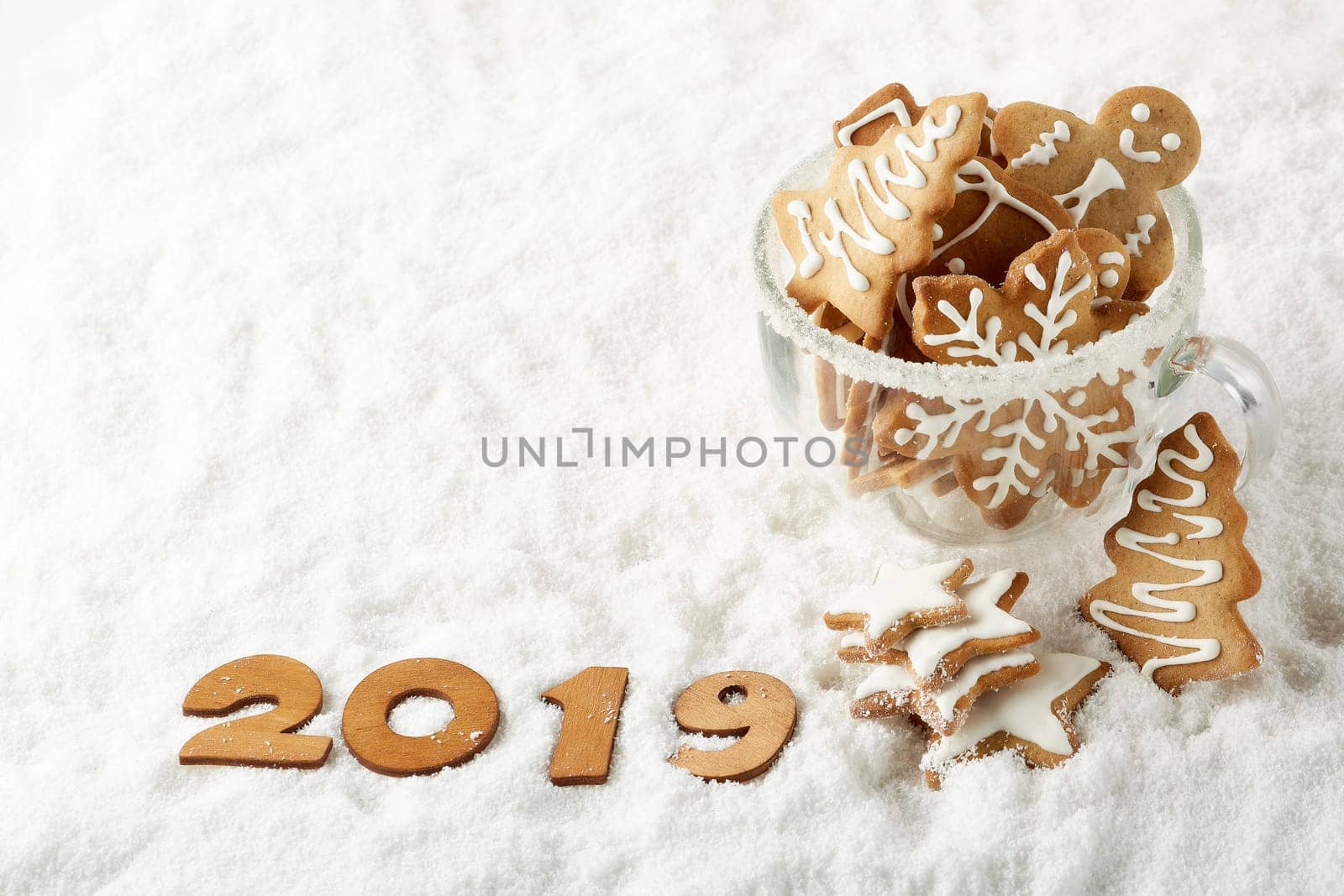Handmade cookies in a glass cup and text 2019 from wooden figure on white winter snow background with copy space. Top view.Horizontal view. New Year and Christmas.