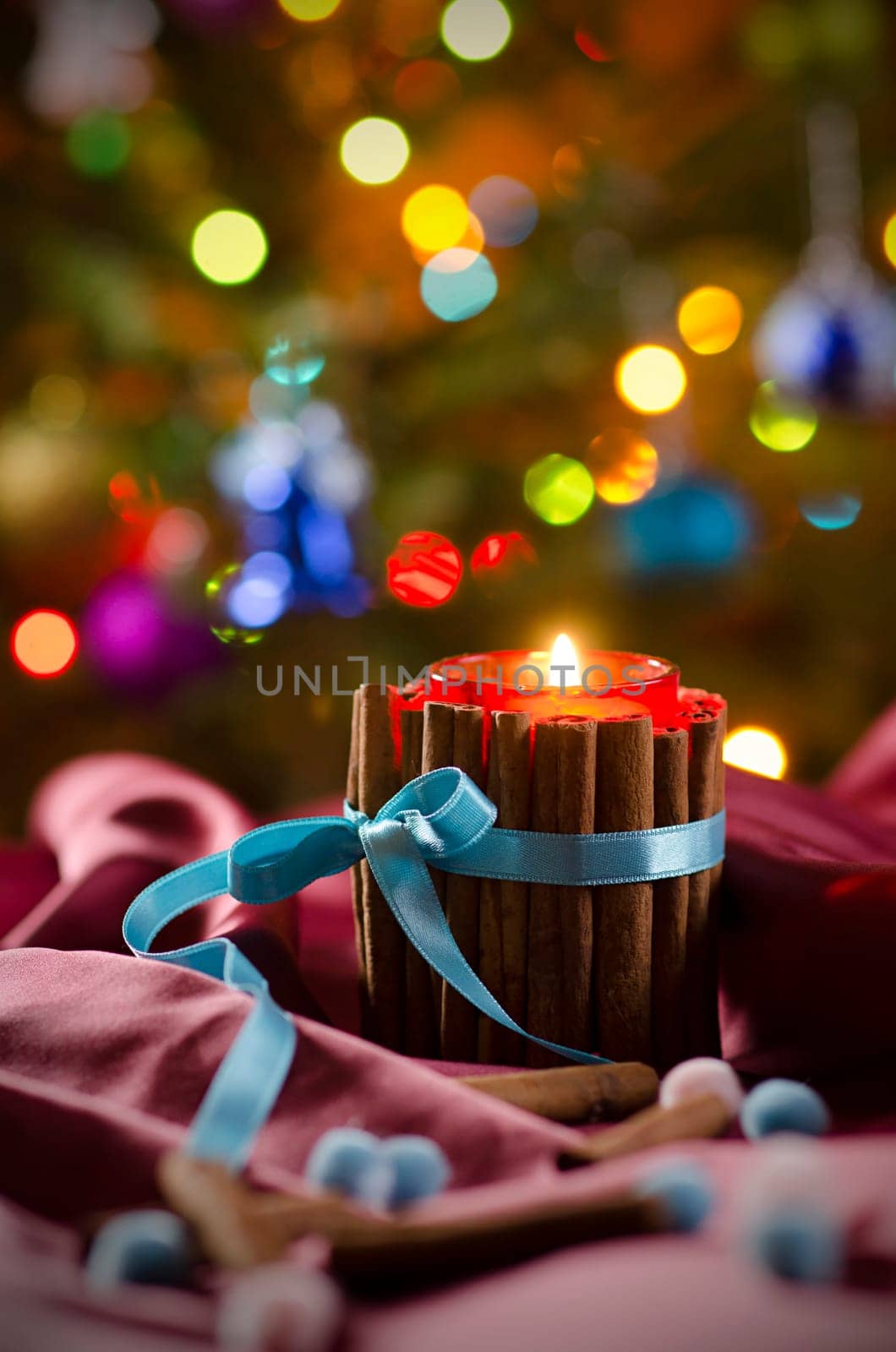 Christmas candle on the background of branches of  Christmas tree and luminous garlands. Burning candle in front of Christmas Tree.