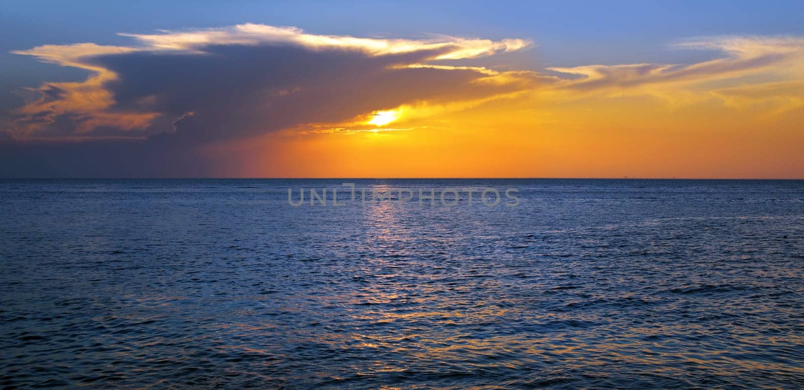 Colorful empty seascape with shiny sea over cloudy sky and sun during sunset in Cozumel, Mexico