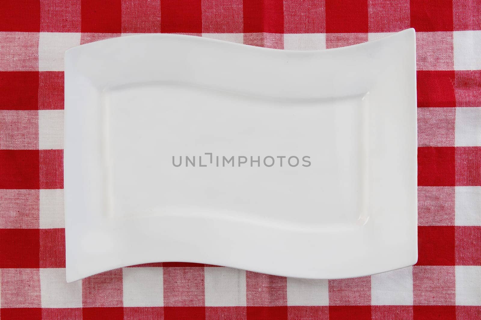Empty white plate on red napkin or tablecloth. Top view. Template for your food and product display montage. Concept food. Copy space.