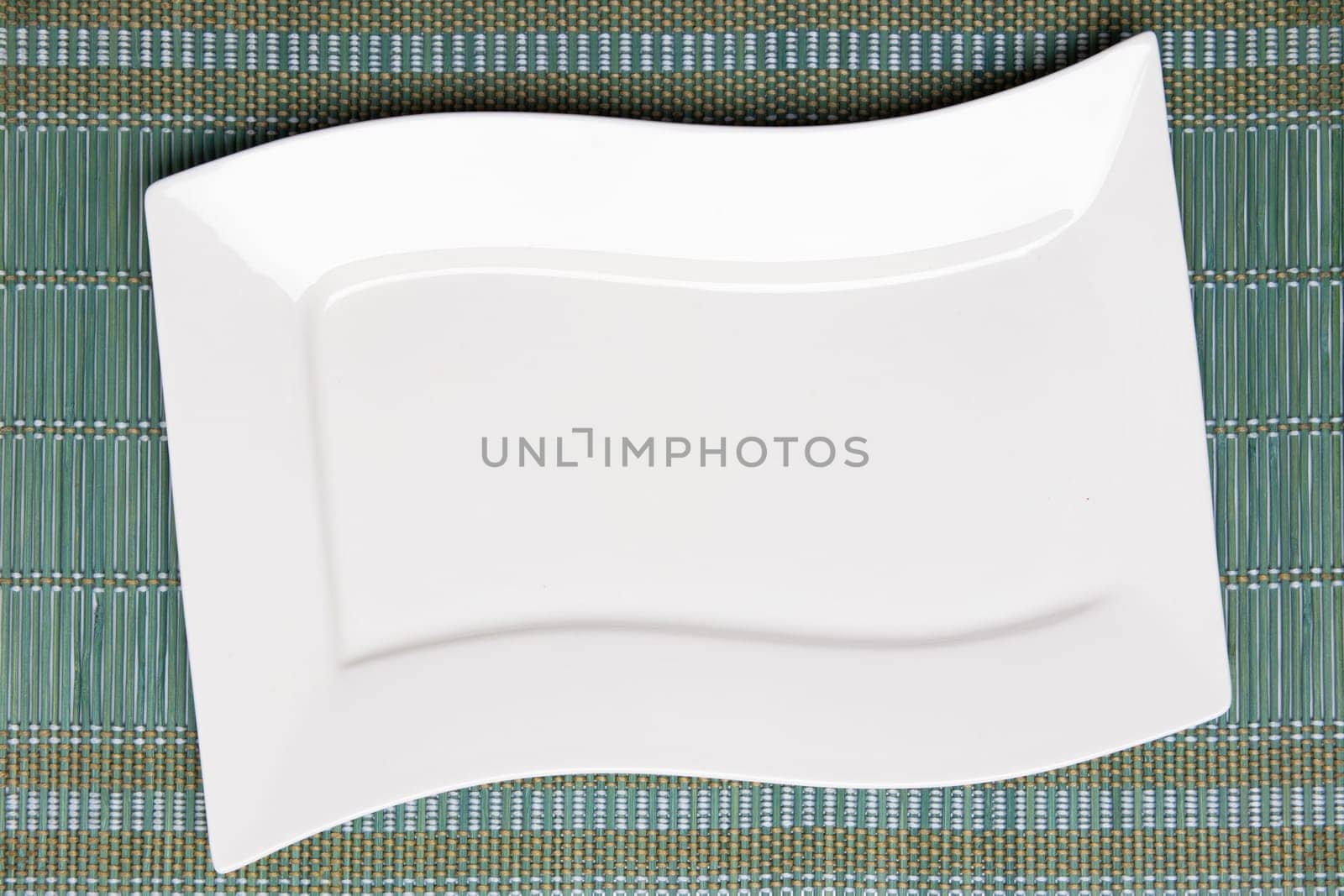 Empty white plate on green napkin or tablecloth. Top view. Template for your food and product display montage. Concept food. Copy space.