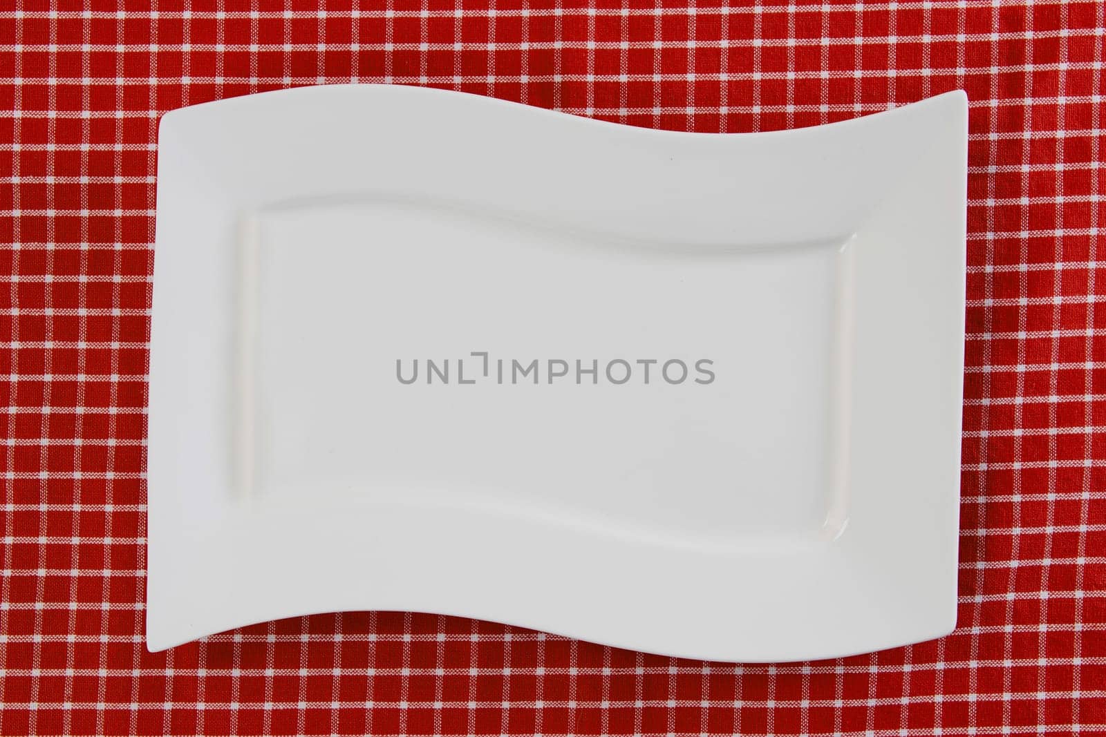 Empty white plate on red napkin or tablecloth. Top view. Template for your food and product display montage. Concept food. Copy space.