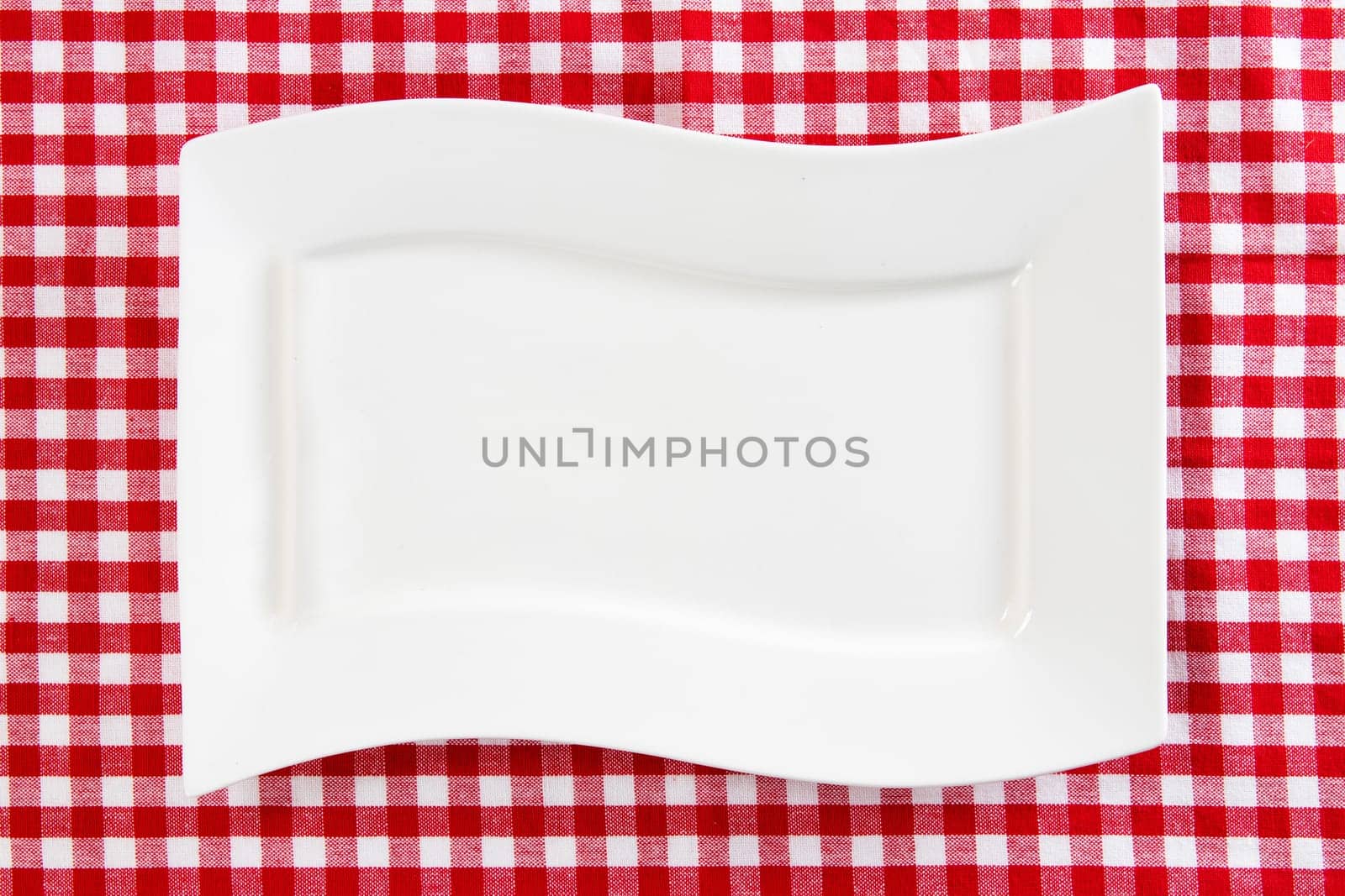Empty white plate on red napkin or tablecloth. Top view. Template for your food and product display montage. Concept food. Copy space.