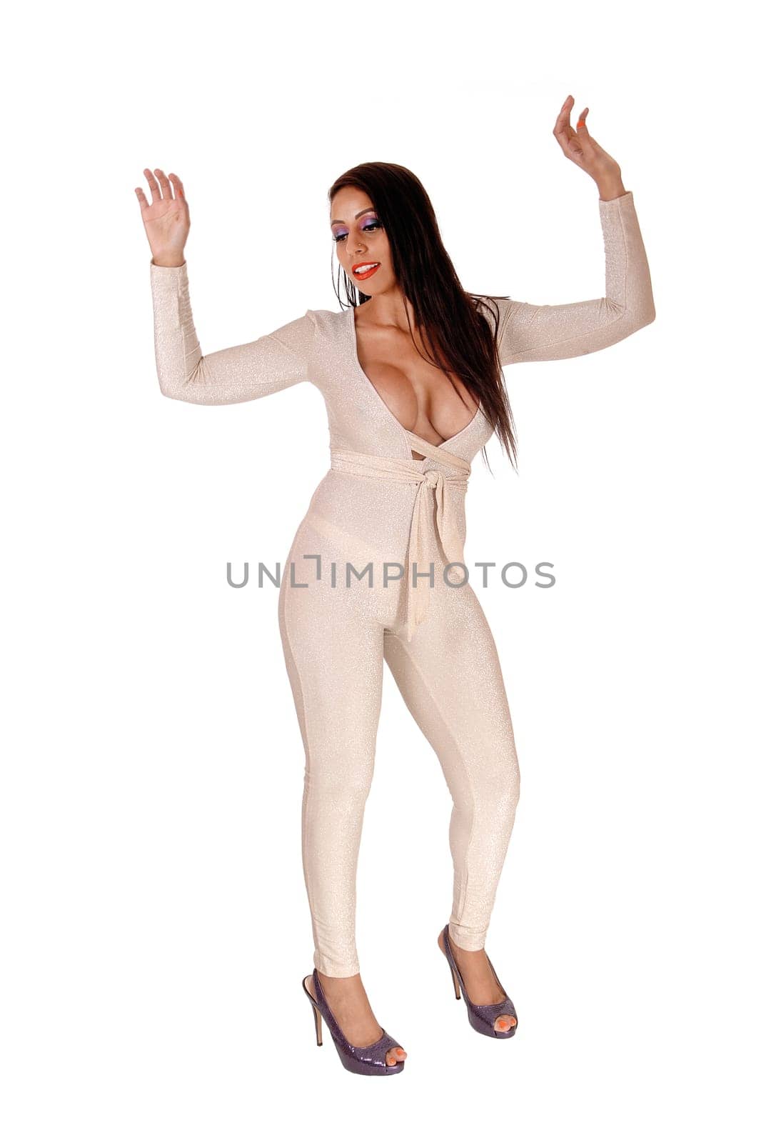 A beautiful young woman standing in a silver color jumpsuit and big.boobs and high heels, dancing in studio, isolated for white background.