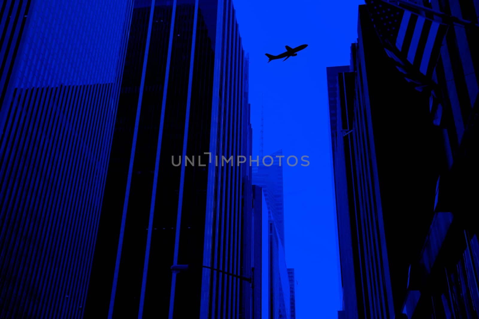 silhouetted flying commercial airplane above buildings.
