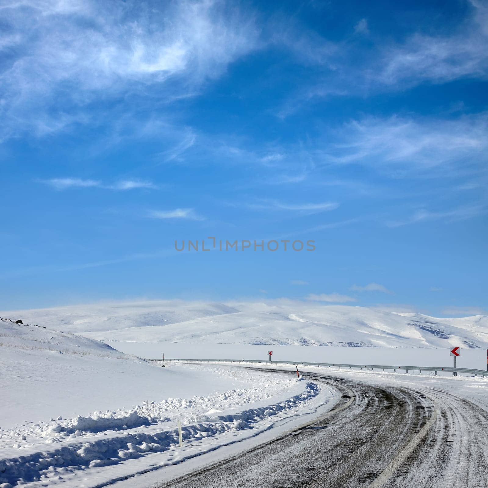Empty frozen asphalt road and snow covered landscape with mountain over blue sky in winter time