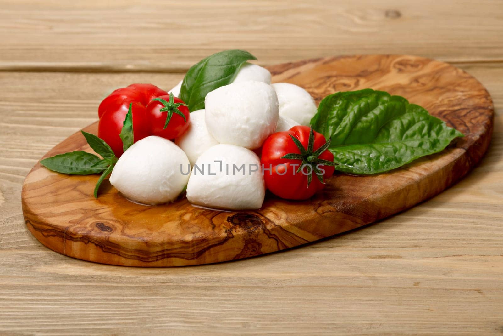 Italian cuisine. Mozzarella, heirloom tomatoes, basil leaves on a wooden serving plate. Selective focus on cheese