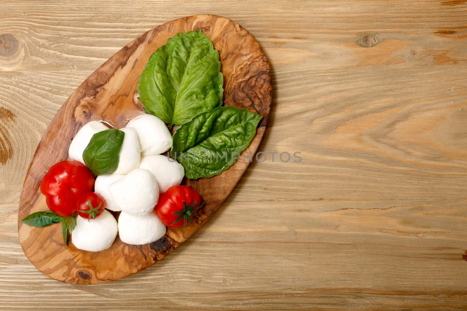 Italian cuisine. Mozzarella, heirloom tomatoes, basil leaves on a wooden serving plate. Flat lay