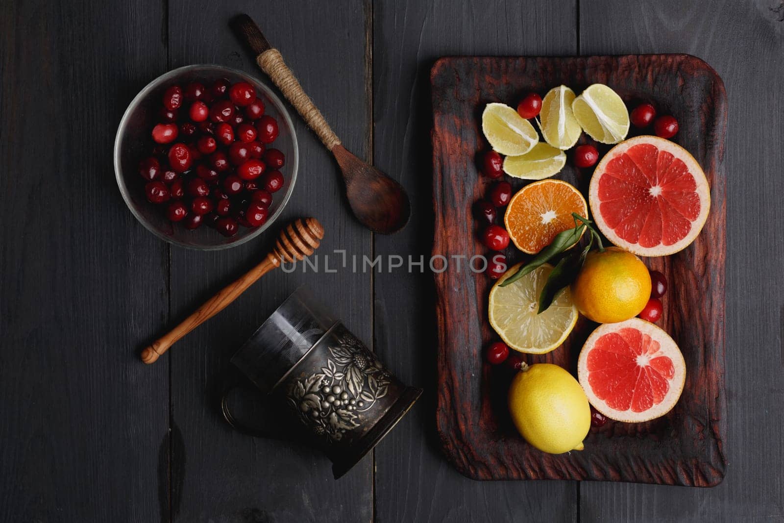Ingredients for hot winter punch,sangria,toddy or mulled wine. Sliced lemon, grapefruit,tangerine, lime and cranberry on a rustic wooden tray over black wooden backdrop