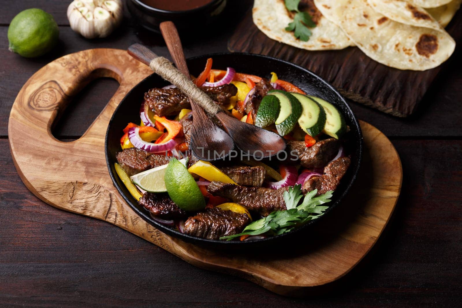Beef fajita with bell peppers. Tortillas, avocado, sauce served with grilled beef and vegetables on skillet. Tex-mex cuisine