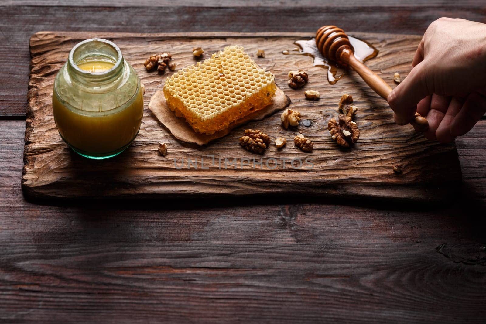 Honey dip,glass jar, honeycomb and walnuts on carved wooden serving plate over burnished wood table. Selective focus