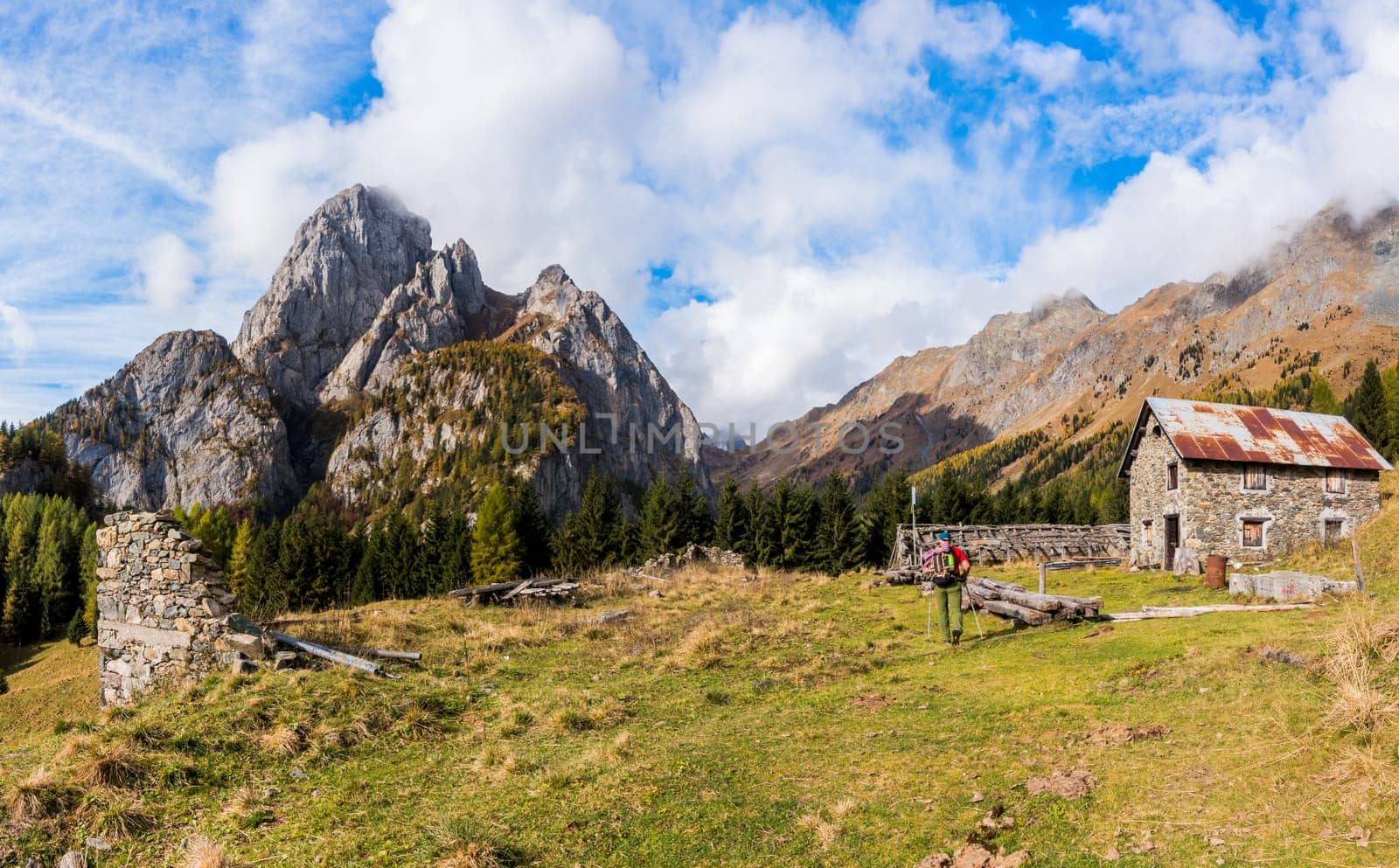 Mountain landscape with blue sky with clouds and ruins of an old farm and a hiker