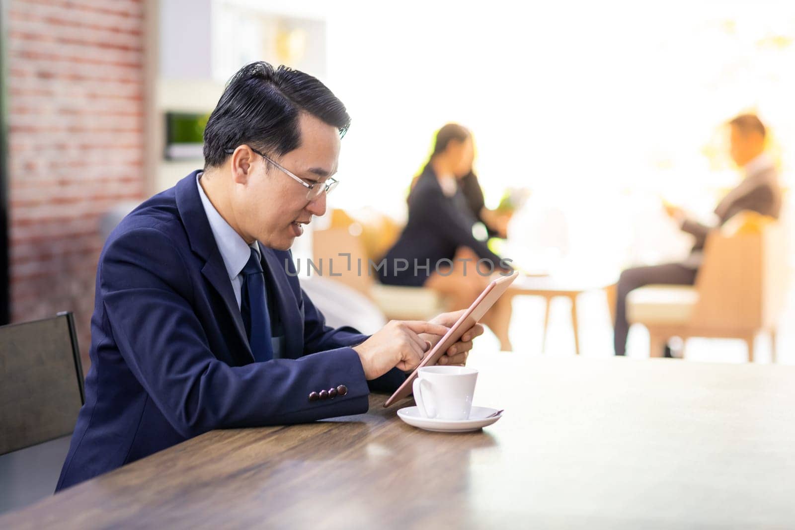 Portrait of Businessman working in cafe with smart phone and tablet with business team in background using for coporate background work