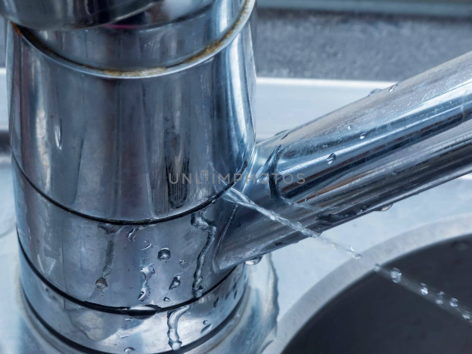 Close-up of a leaking faucet with jetting out the jet of water on a sink at the window.