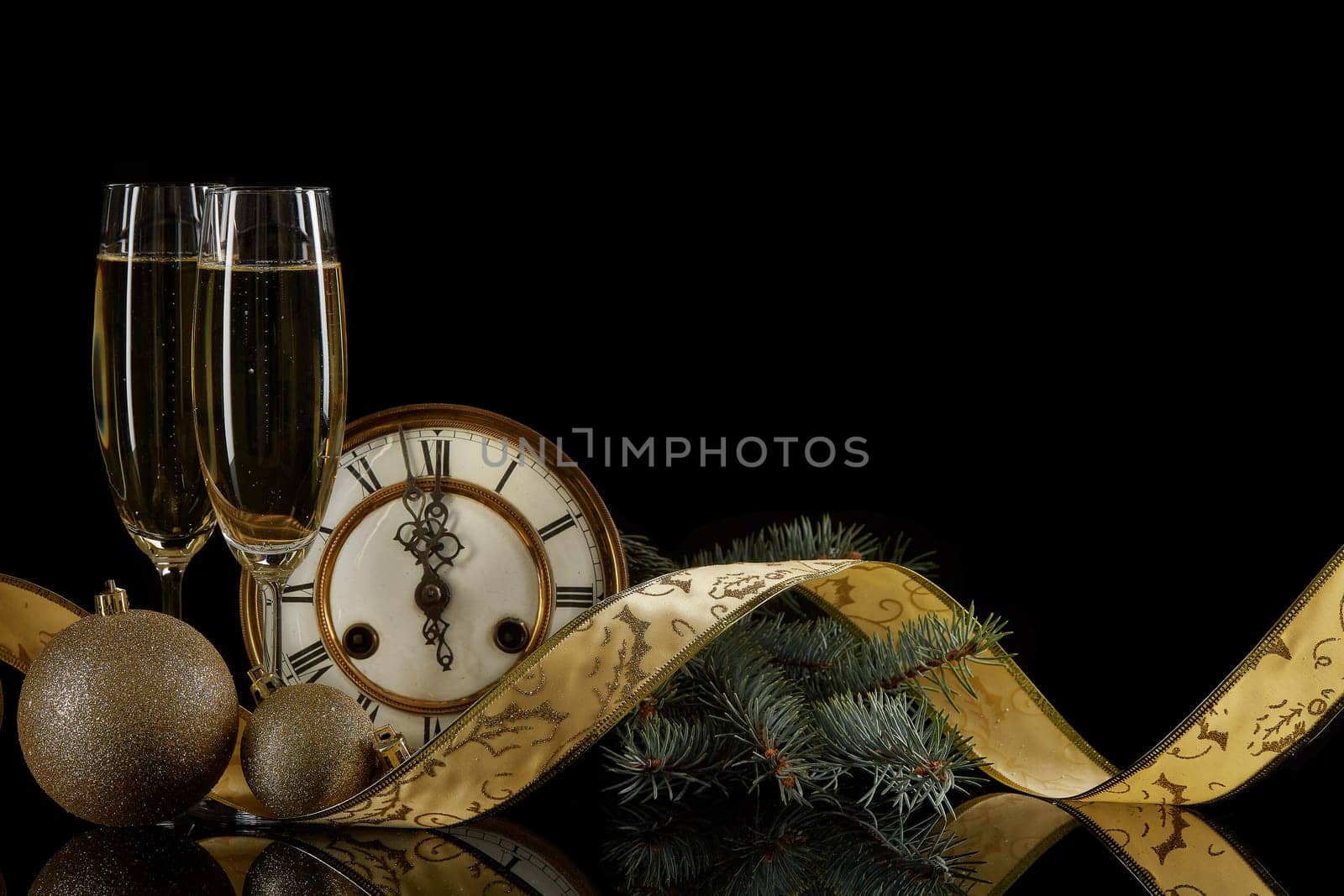Two wineglasses with champange, fir tree branches, clock and christmas ornament on a black background with reflection. Copy space. Christmas and New Year background